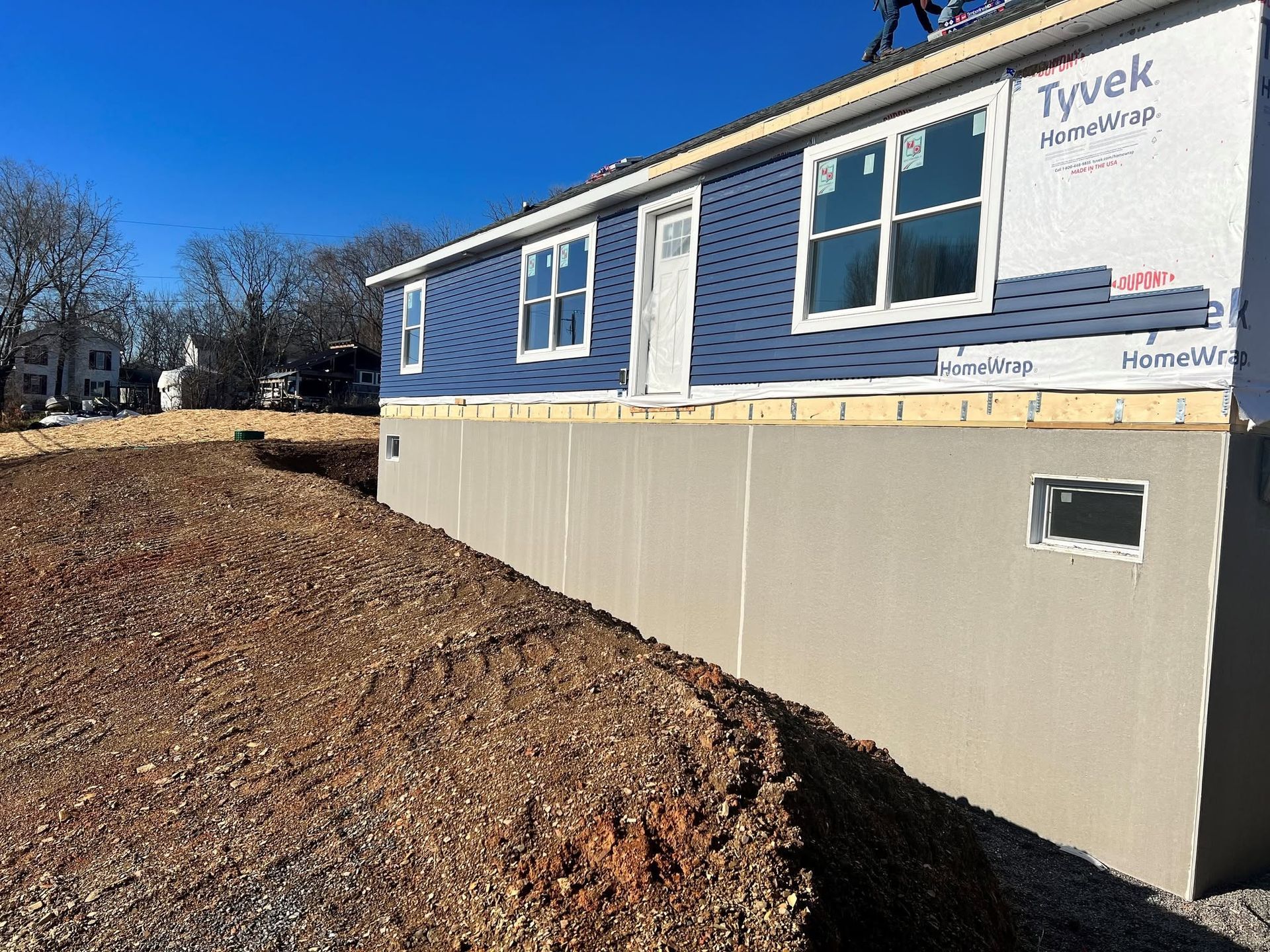 Blue house under construction with beige foundation and dirt slope in the foreground