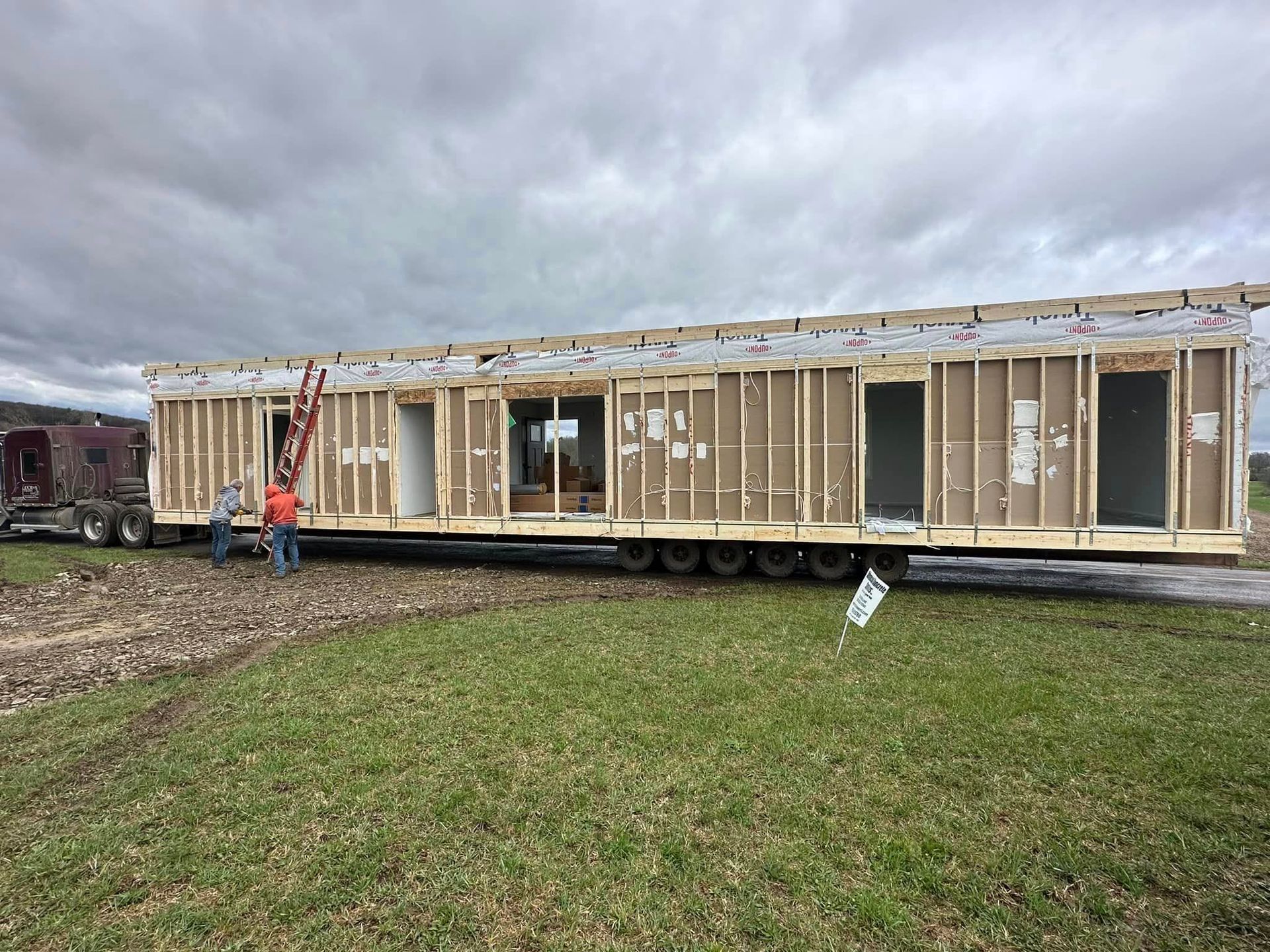Partially built modular home on a trailer with exposed framing and two workers outside