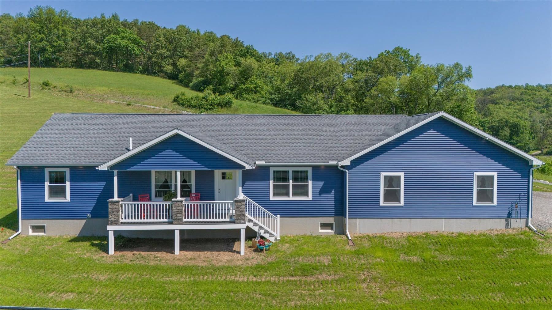 Blue ranch-style house with a front porch on a grassy hillside under a clear sky