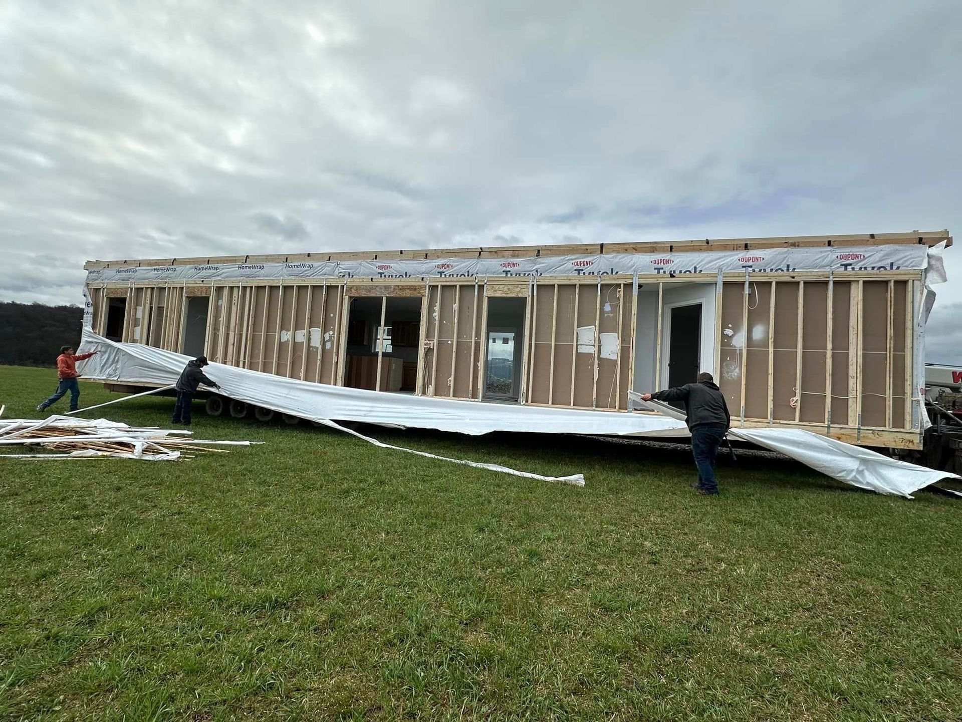 Damaged mobile home with collapsed siding and two people assessing storm damage on a grassy lot