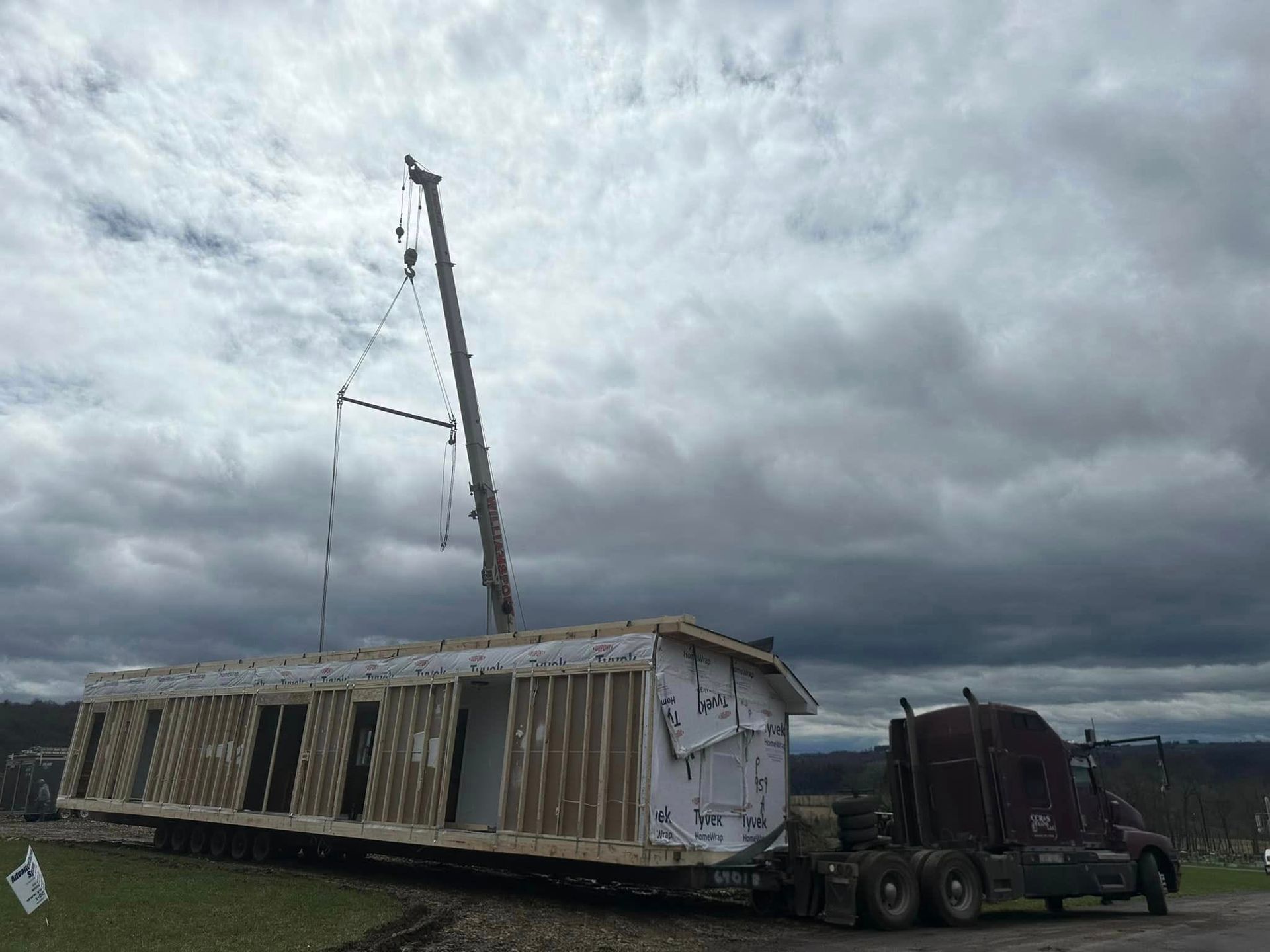 Mobile home being lifted onto a truck under dark storm clouds, tilted on its side.