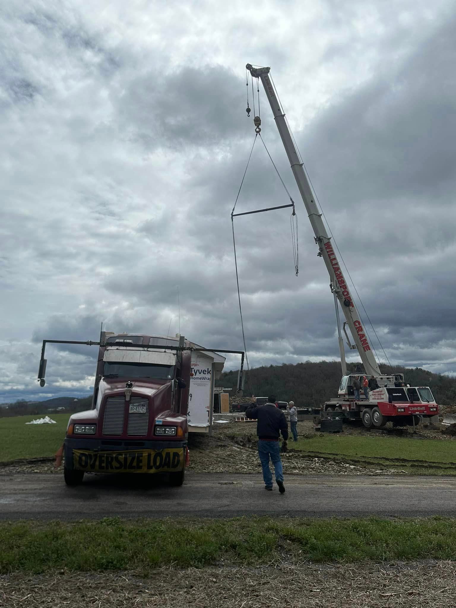 Crane lifting a tall metal frame beside a truck in an open field, with a person standing nearby.