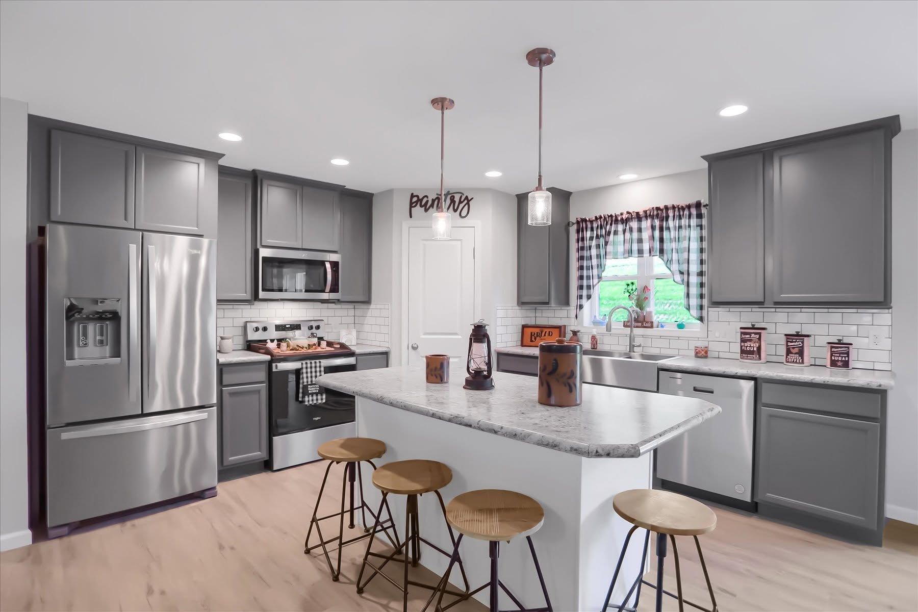 Modern gray kitchen with stainless steel appliances, white island, and four stools by a window.