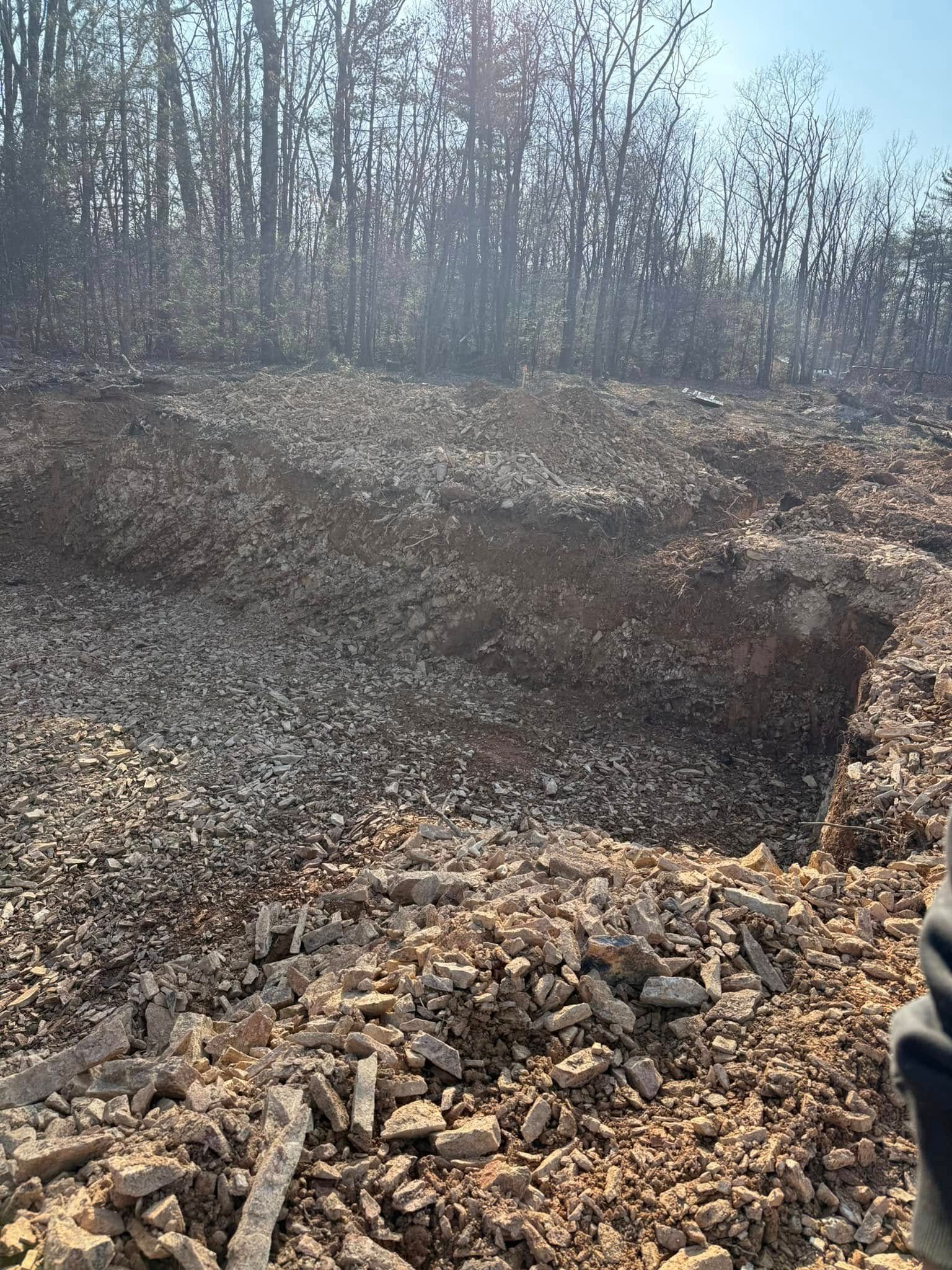 Dirt construction site with an excavated trench, rocky soil, and bare trees in the background