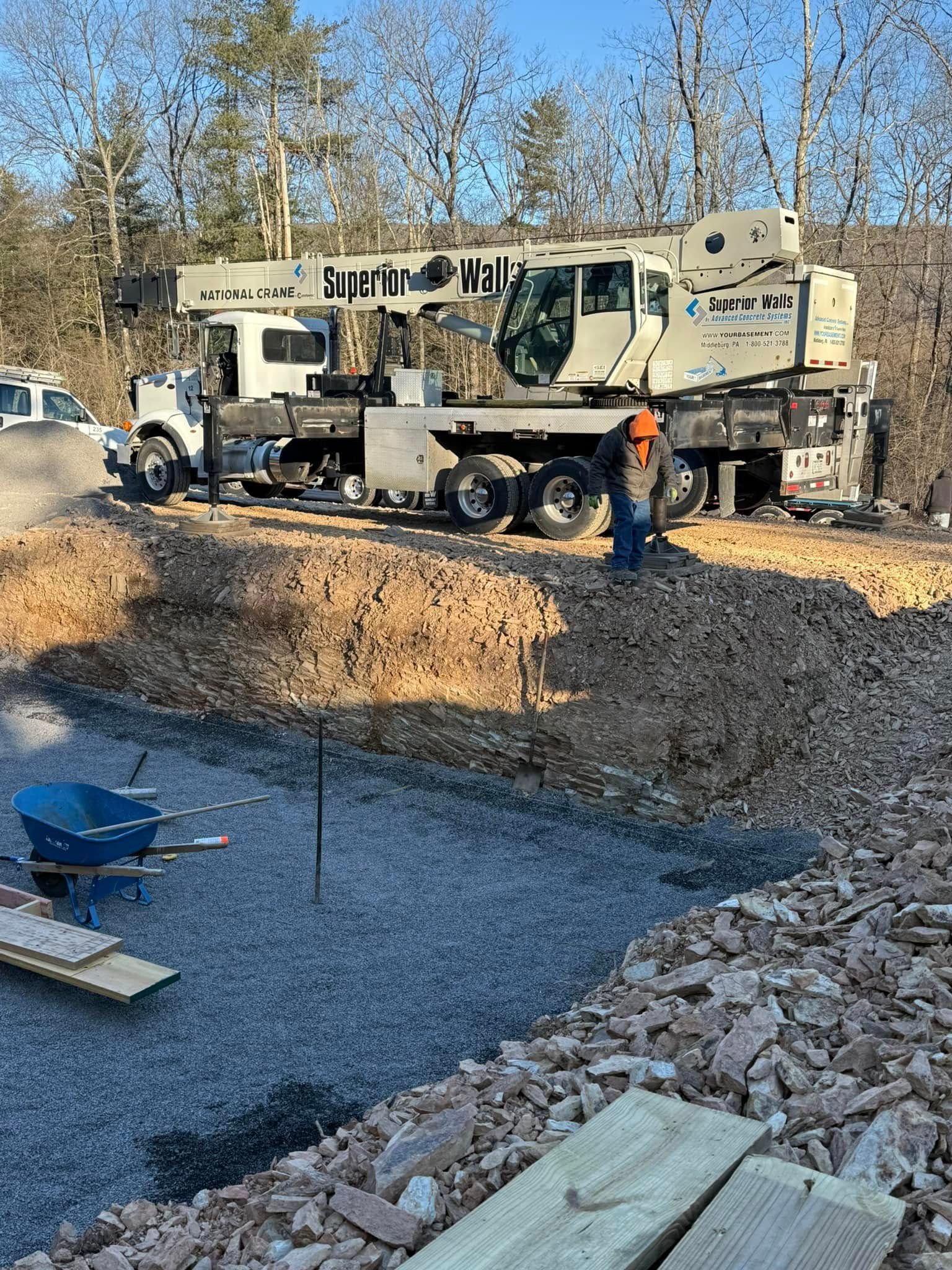 Construction truck on gravel worksite with two workers and a large boom arm under bare trees