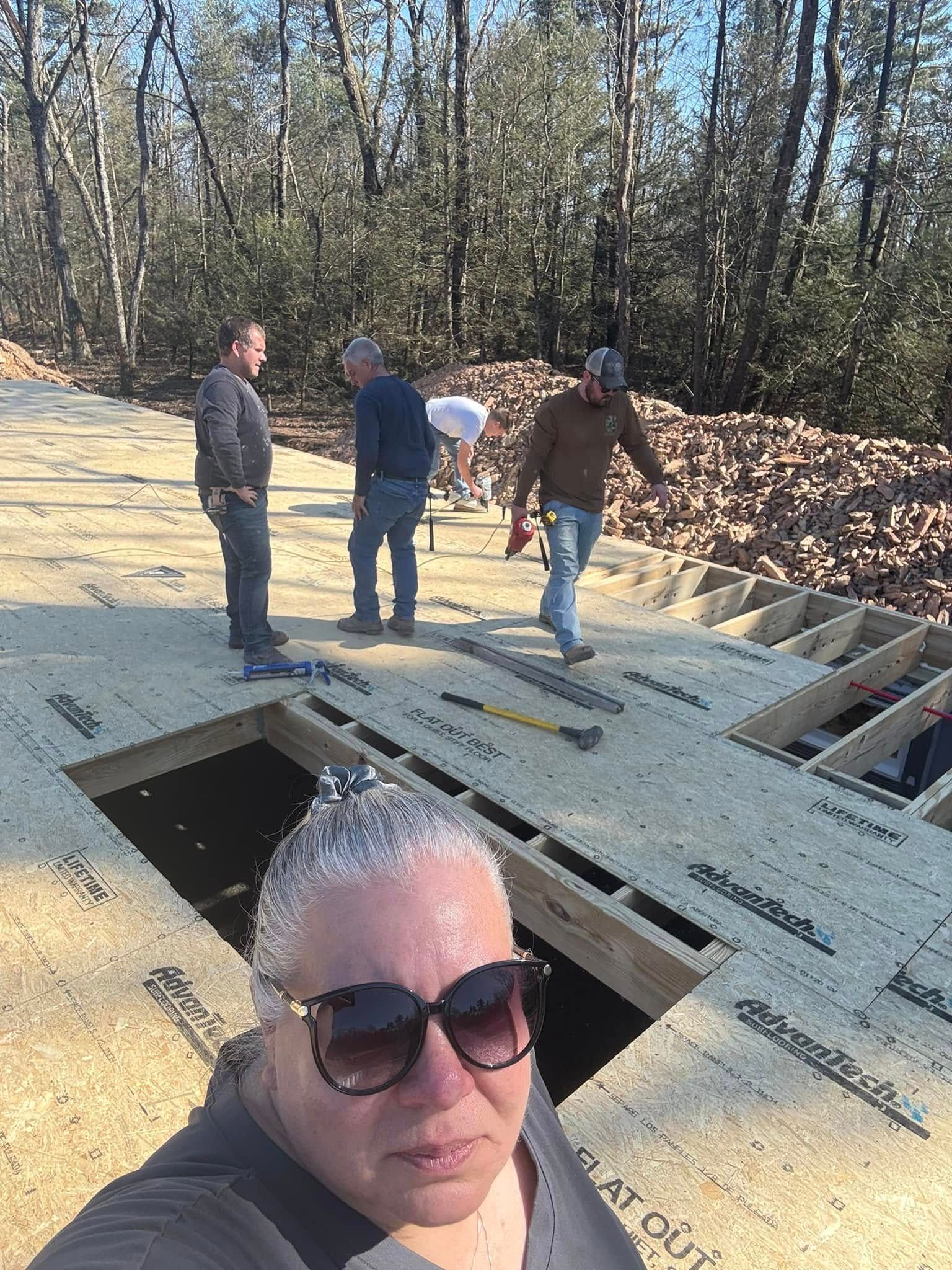 People standing on a rooftop under construction with open skylight cutouts, one person in the foreground taking a selfie