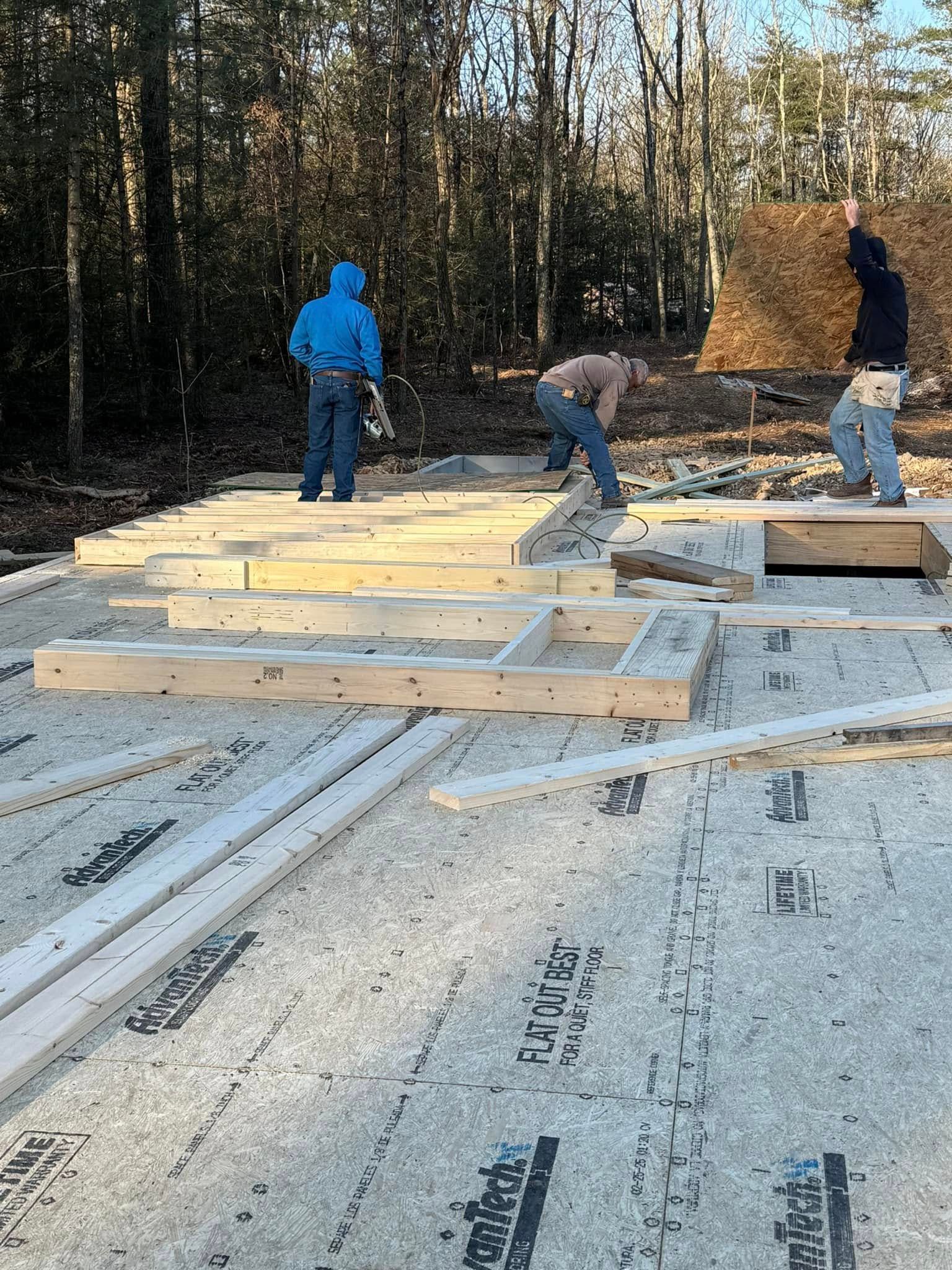 Workers framing a wooden floor on a concrete foundation in a wooded construction site
