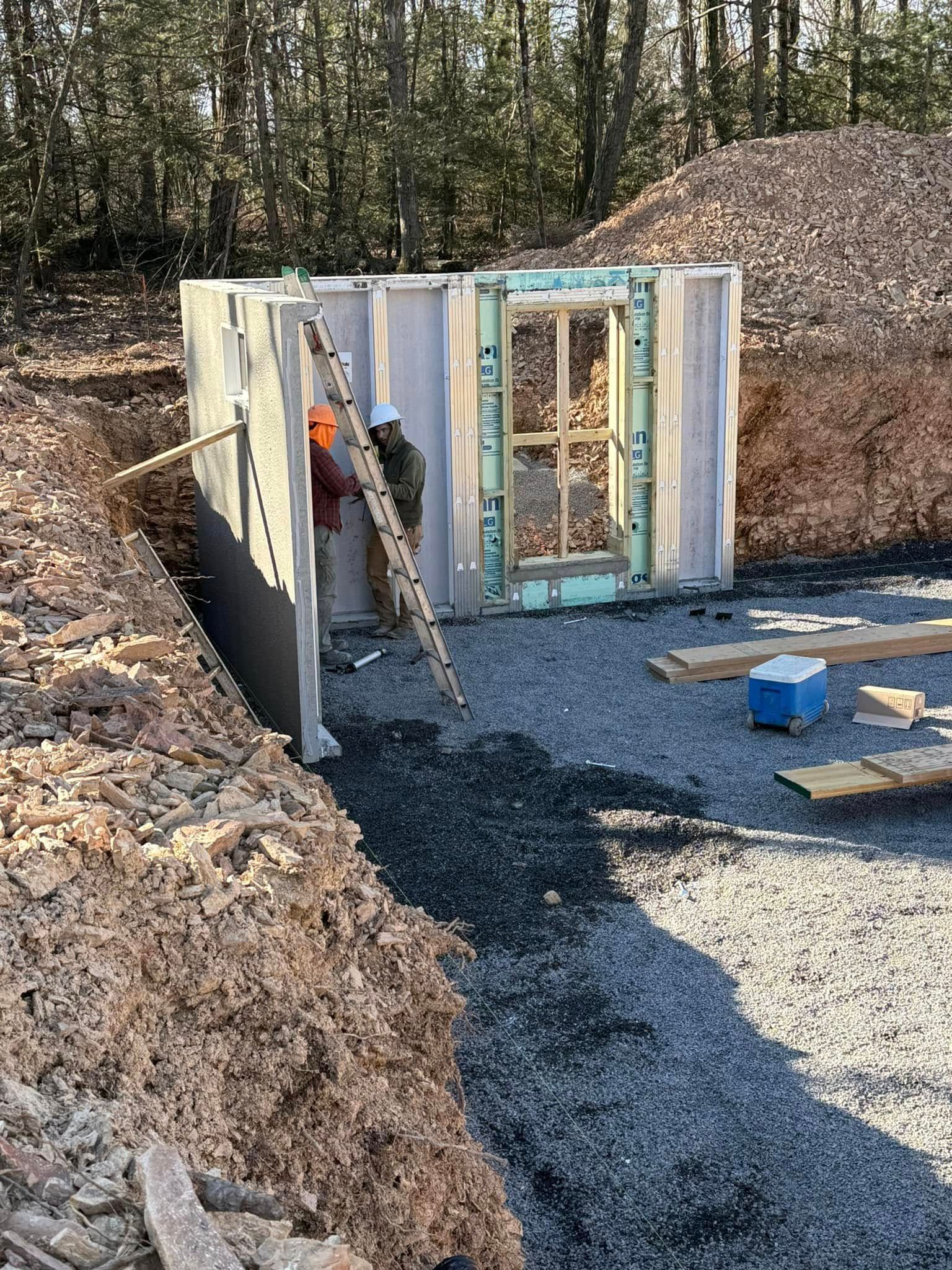 Foundation excavation with foam wall forms, gravel floor, and a worker using a power tool beside a soil berm