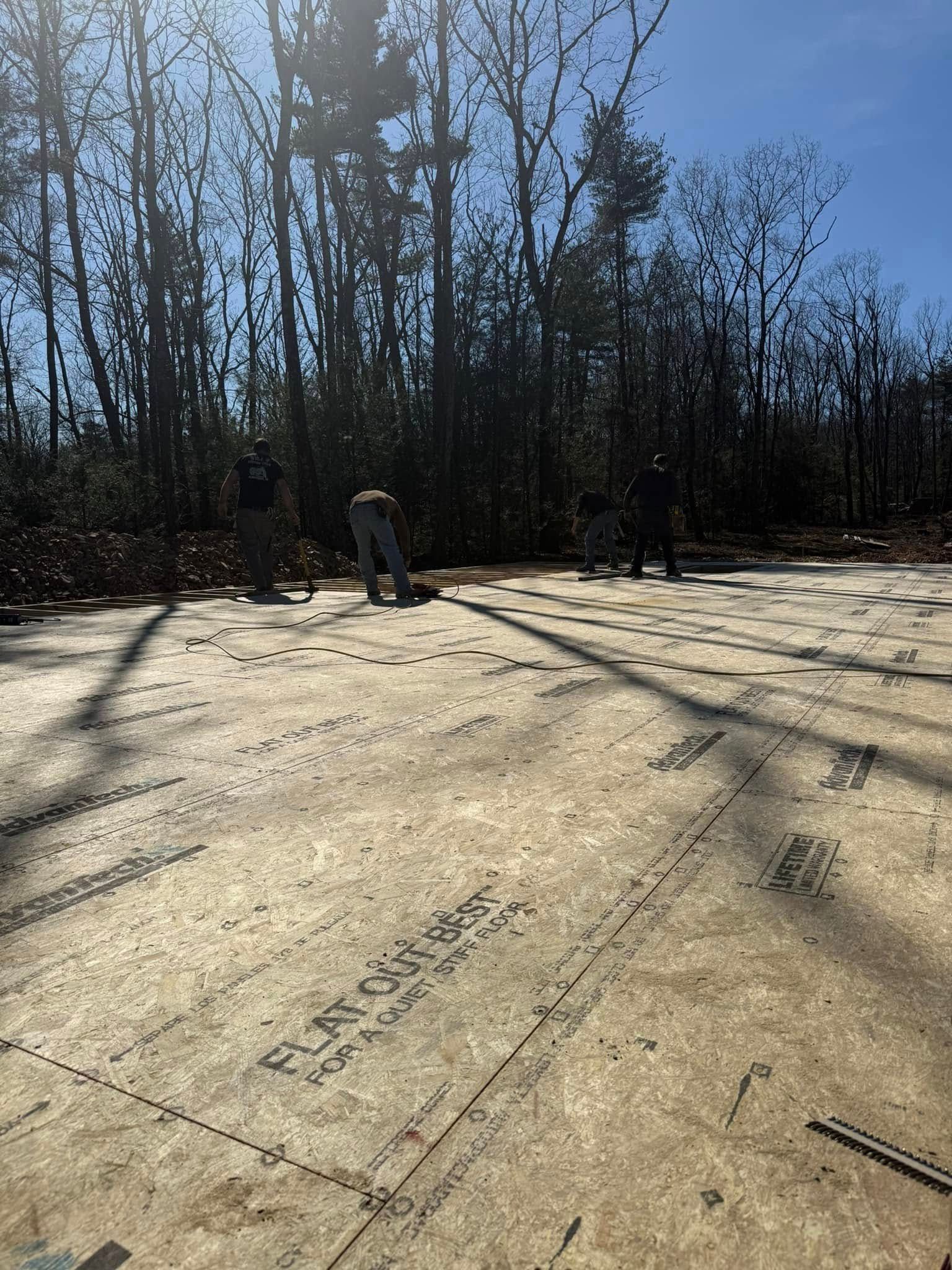 Wooden foundation under construction in a sunny wooded area, with workers in the background.
