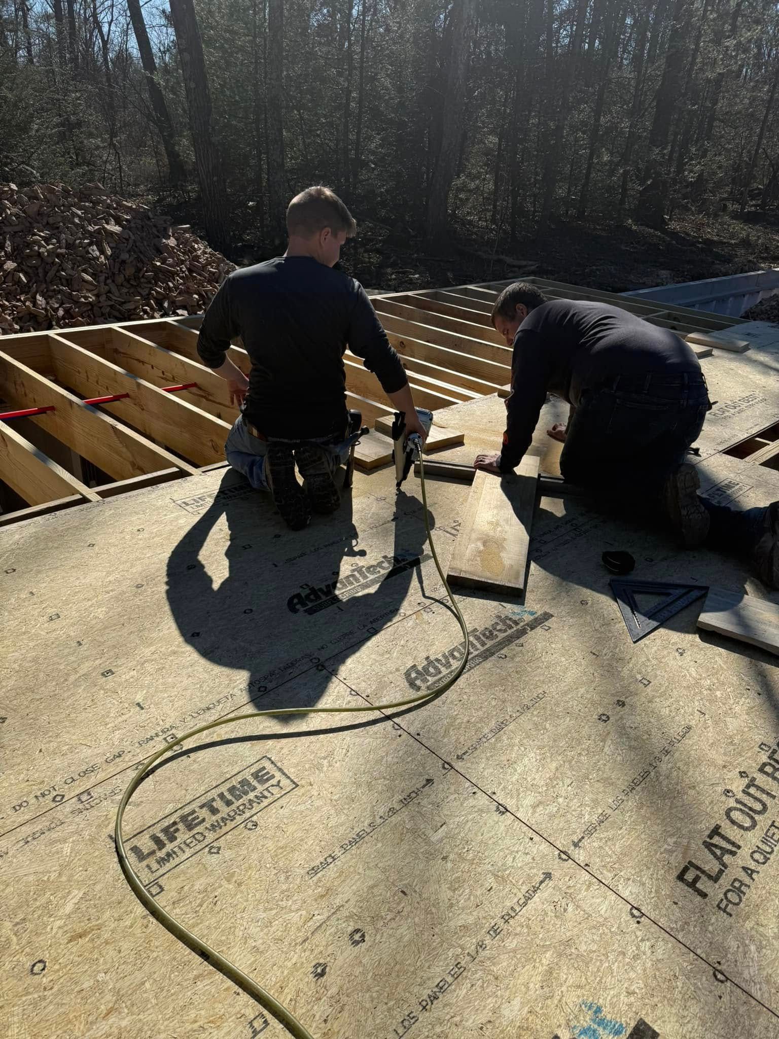 Two workers installing roofing underlayment on a sloped roof in bright sunlight