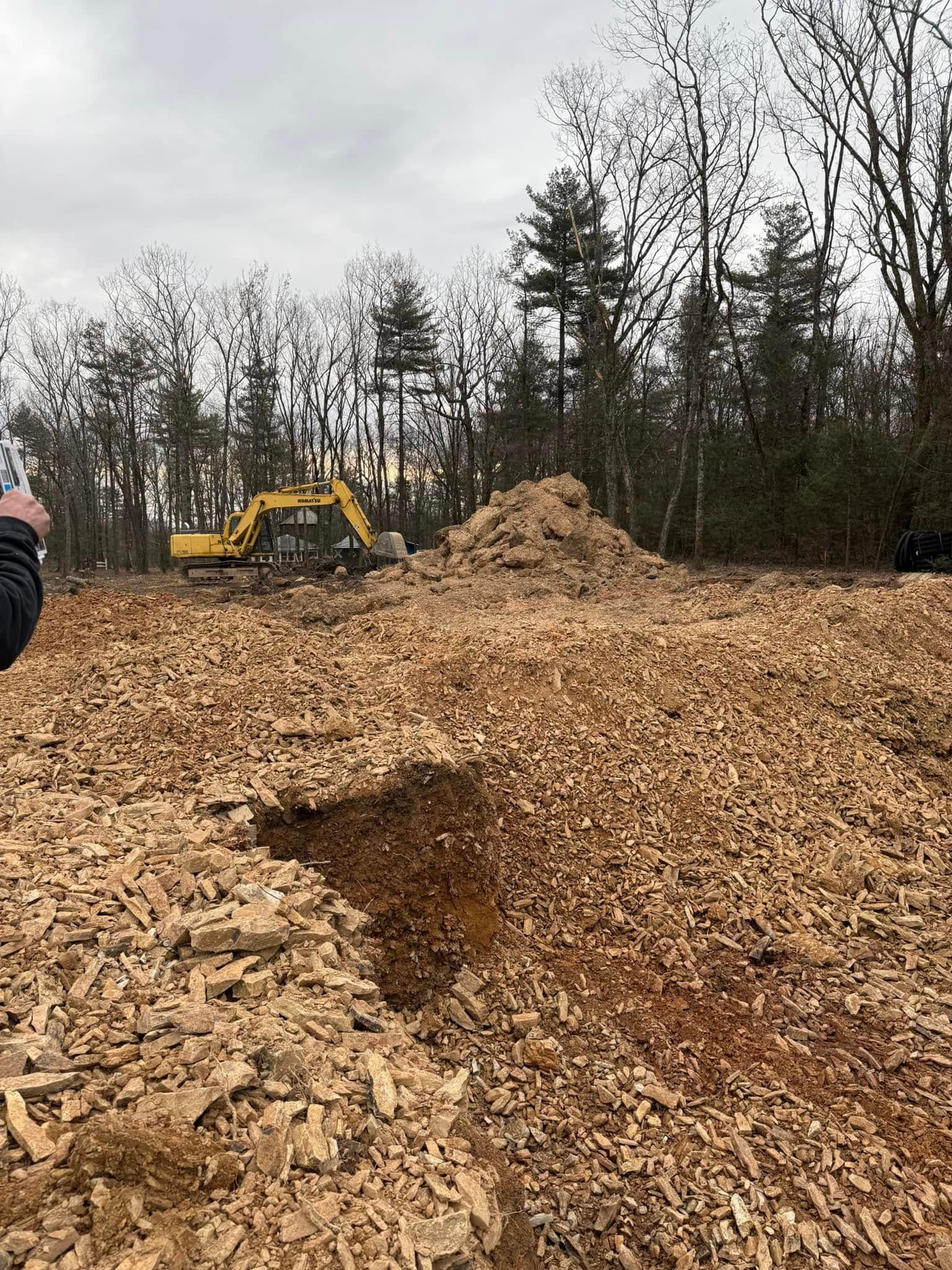 Bulldozer on a large wood-chip pile beside a muddy clearing and trees