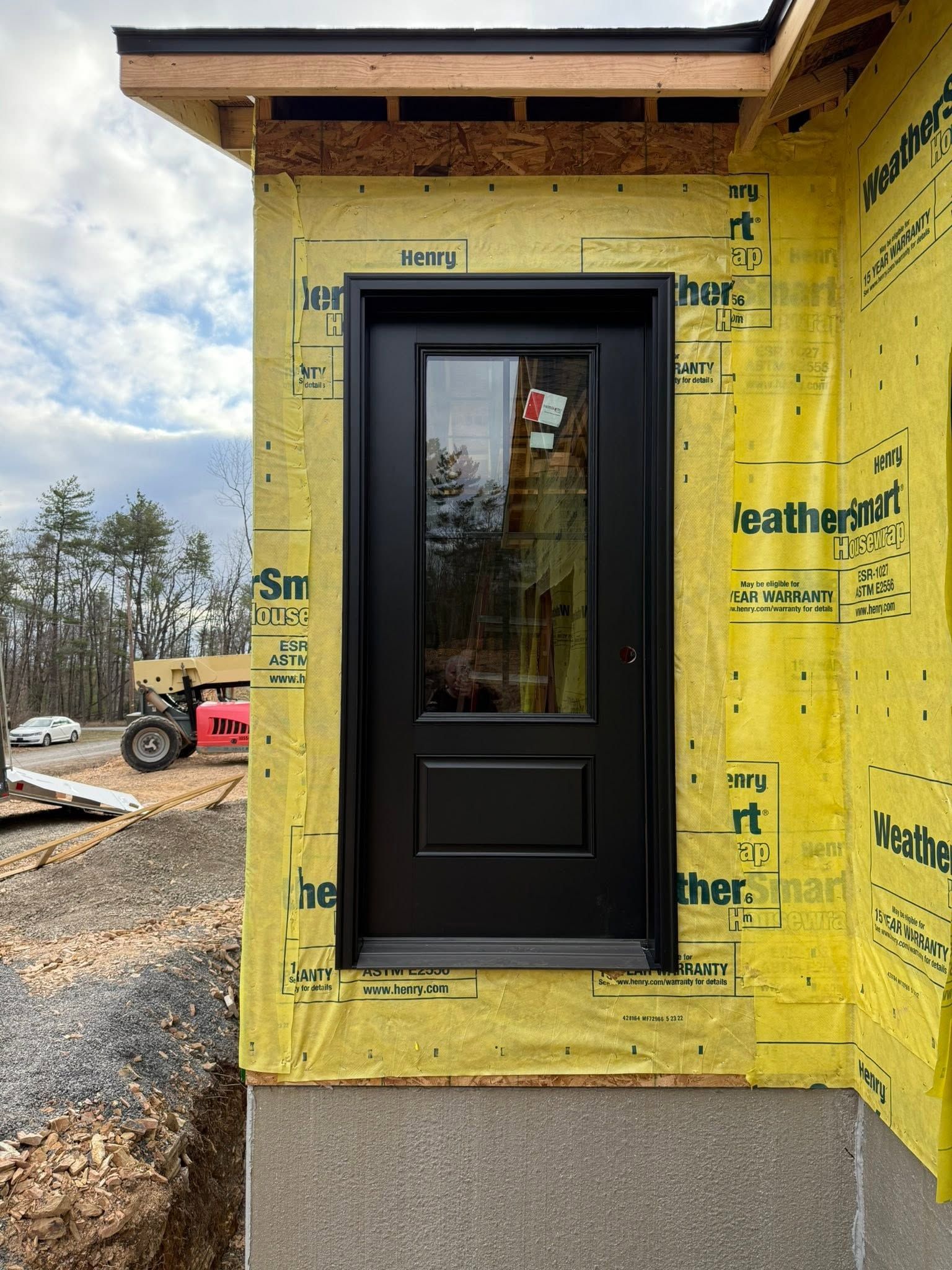 Black front door in a yellow house under construction with exposed framing and house wrap