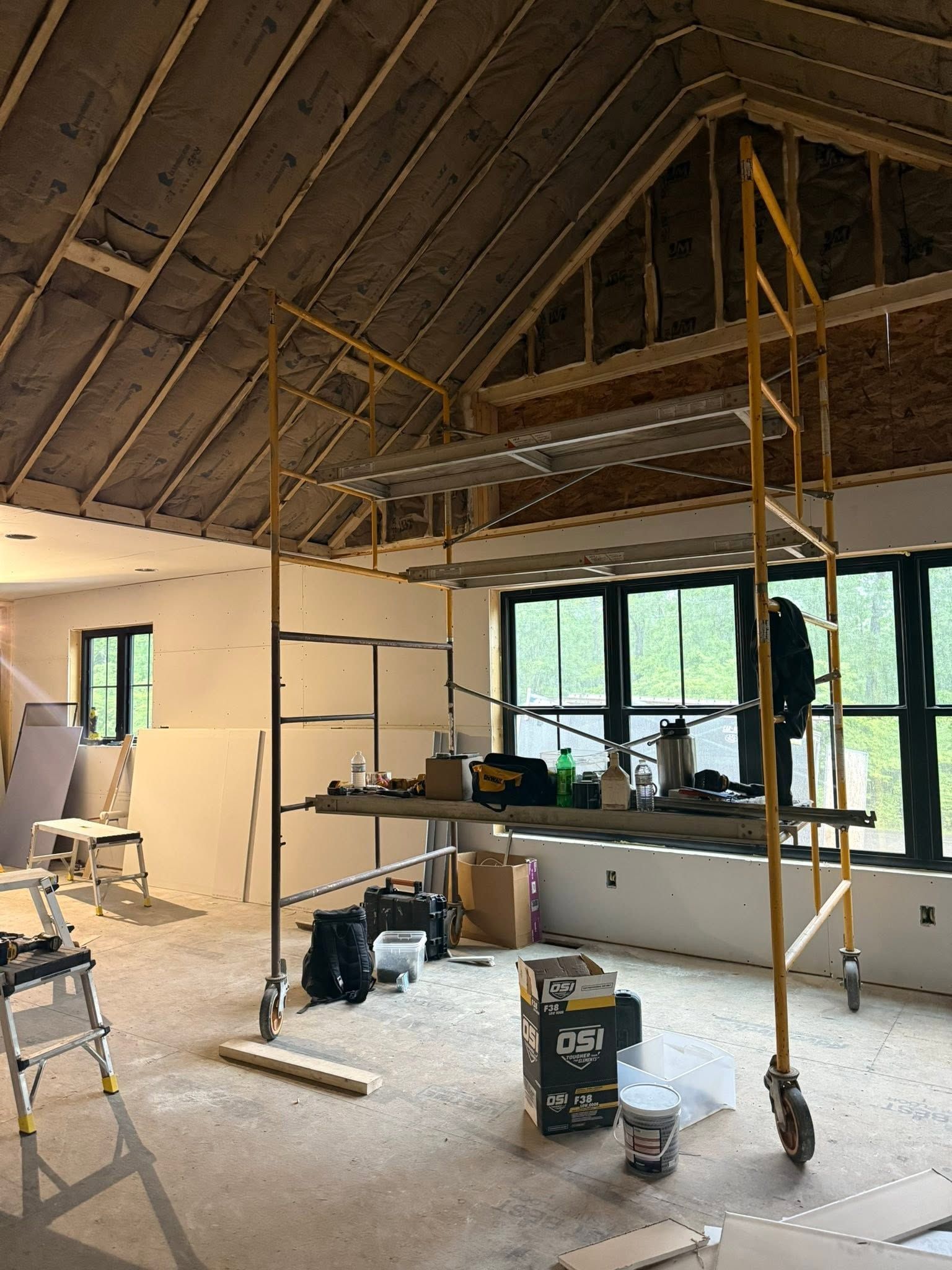 Interior under renovation with scaffolding, exposed ceiling beams, and construction materials on the floor.