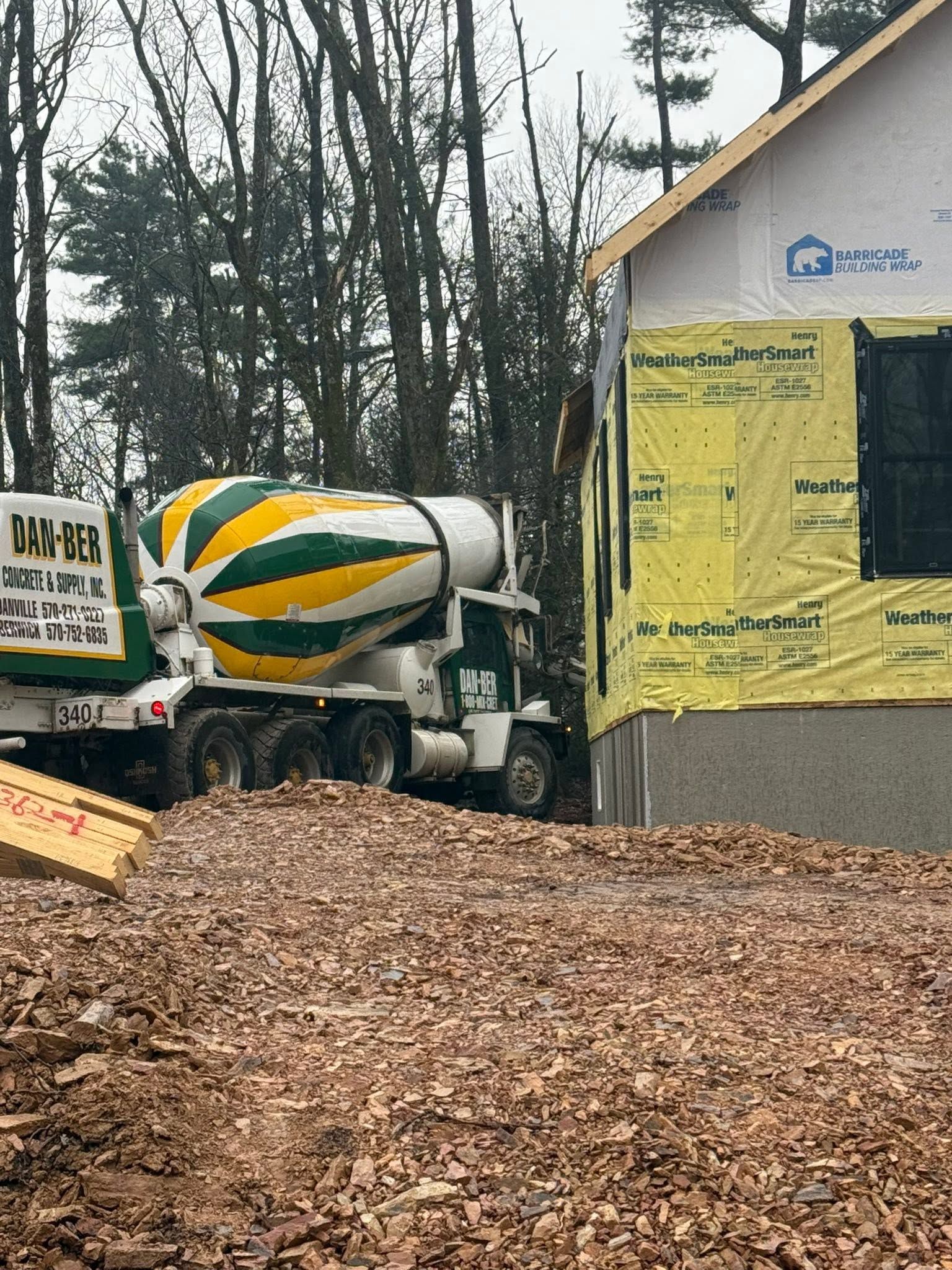 Cement mixer truck at a house under construction, with yellow wrap and leaf-covered ground.