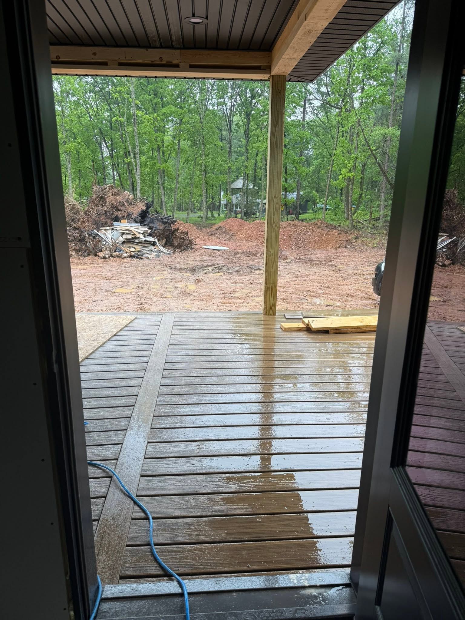 Wet wooden deck leading to a wooded backyard, viewed from a doorway after rain.
