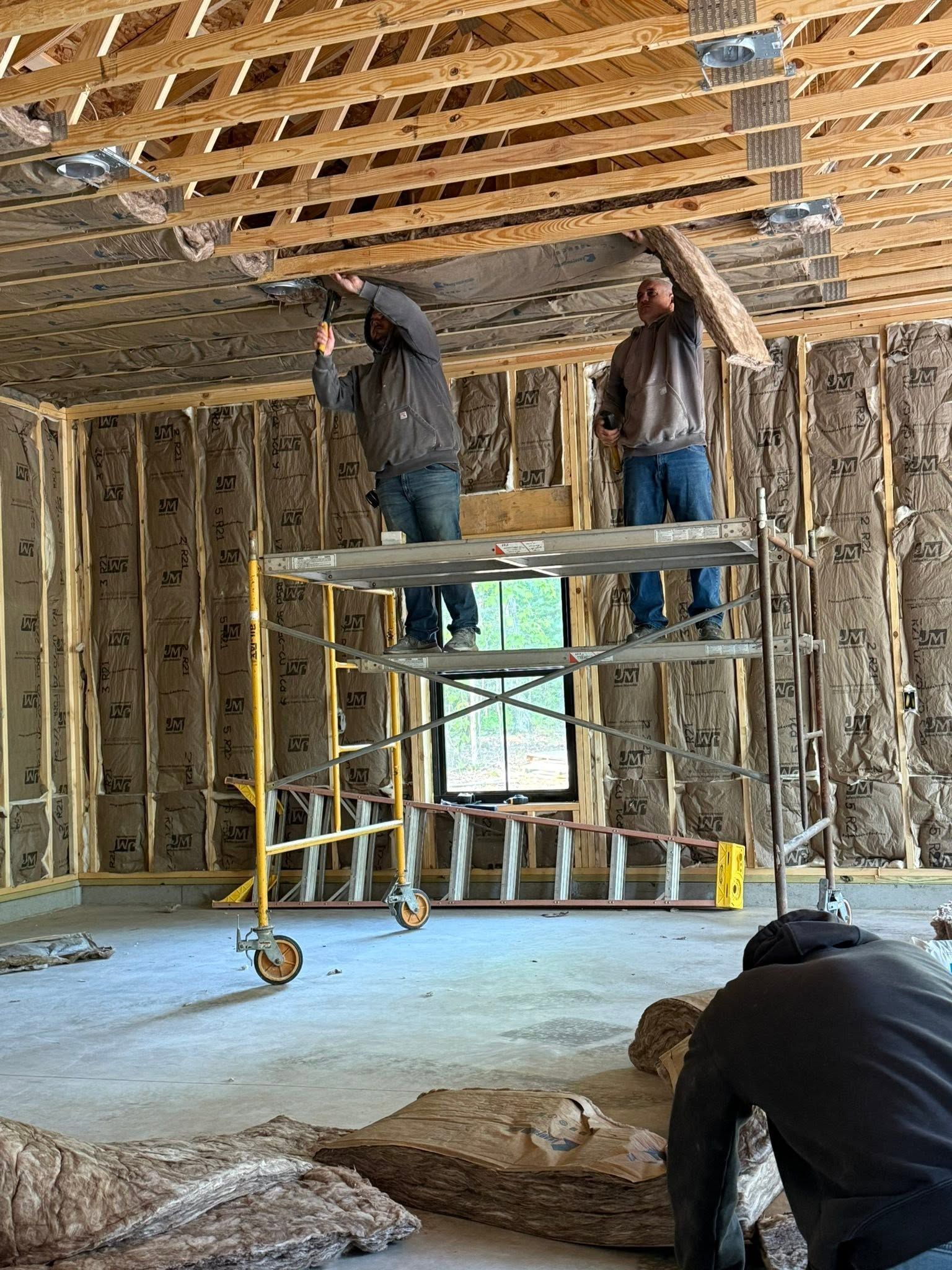 Two workers on scaffolding installing ceiling framing in an unfinished room