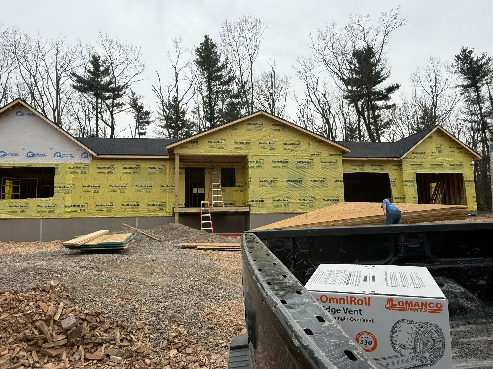 Partially built house with yellow siding, gravel yard, and construction materials in front
