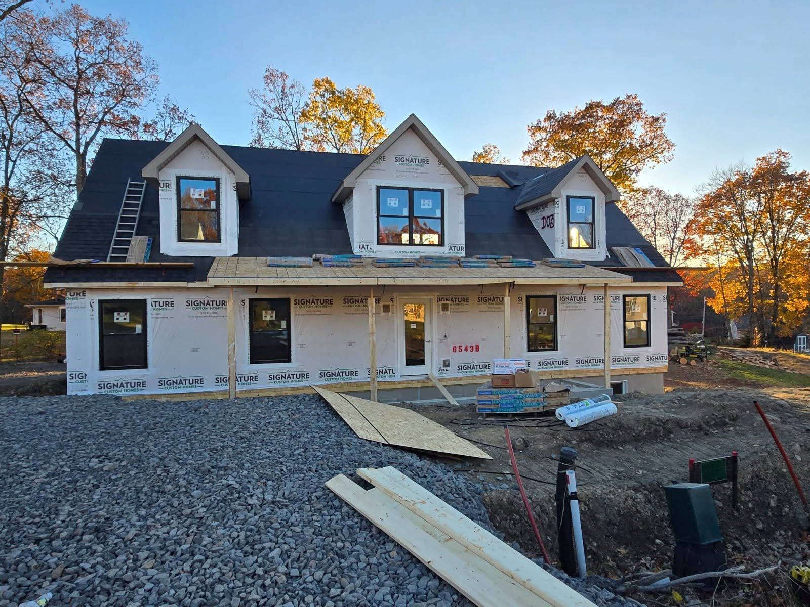 New house under construction with white siding, dark roof, and gravel driveway in front