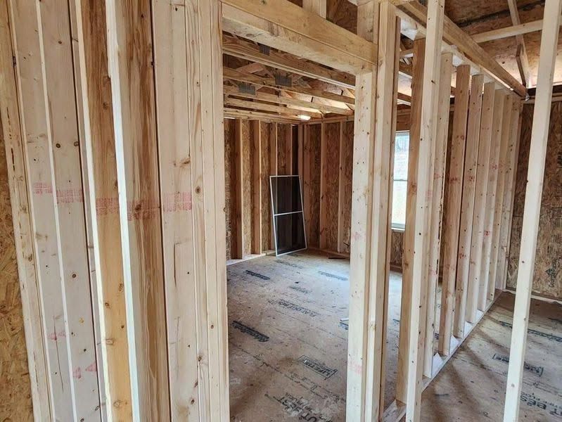 Unfinished wooden house interior with exposed framing and subfloor, viewed down a narrow hallway