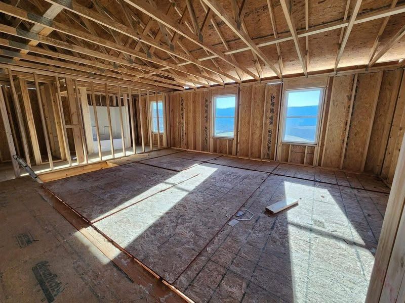 Unfinished house interior with exposed wooden framing, plywood floor, and sunlight through windows