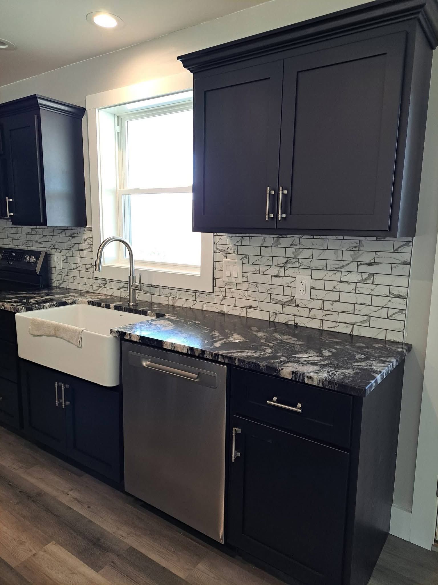 Modern kitchen with dark cabinets, white backsplash, gray countertops, and a stainless sink and dishwasher.