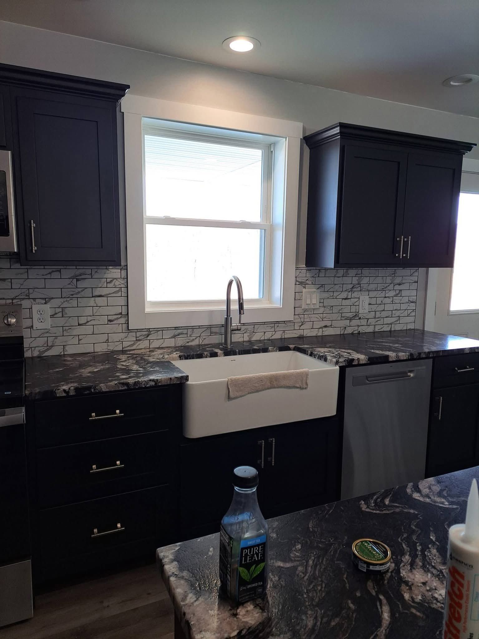 Modern kitchen with dark cabinets, white farmhouse sink, and a bright window over the counter.