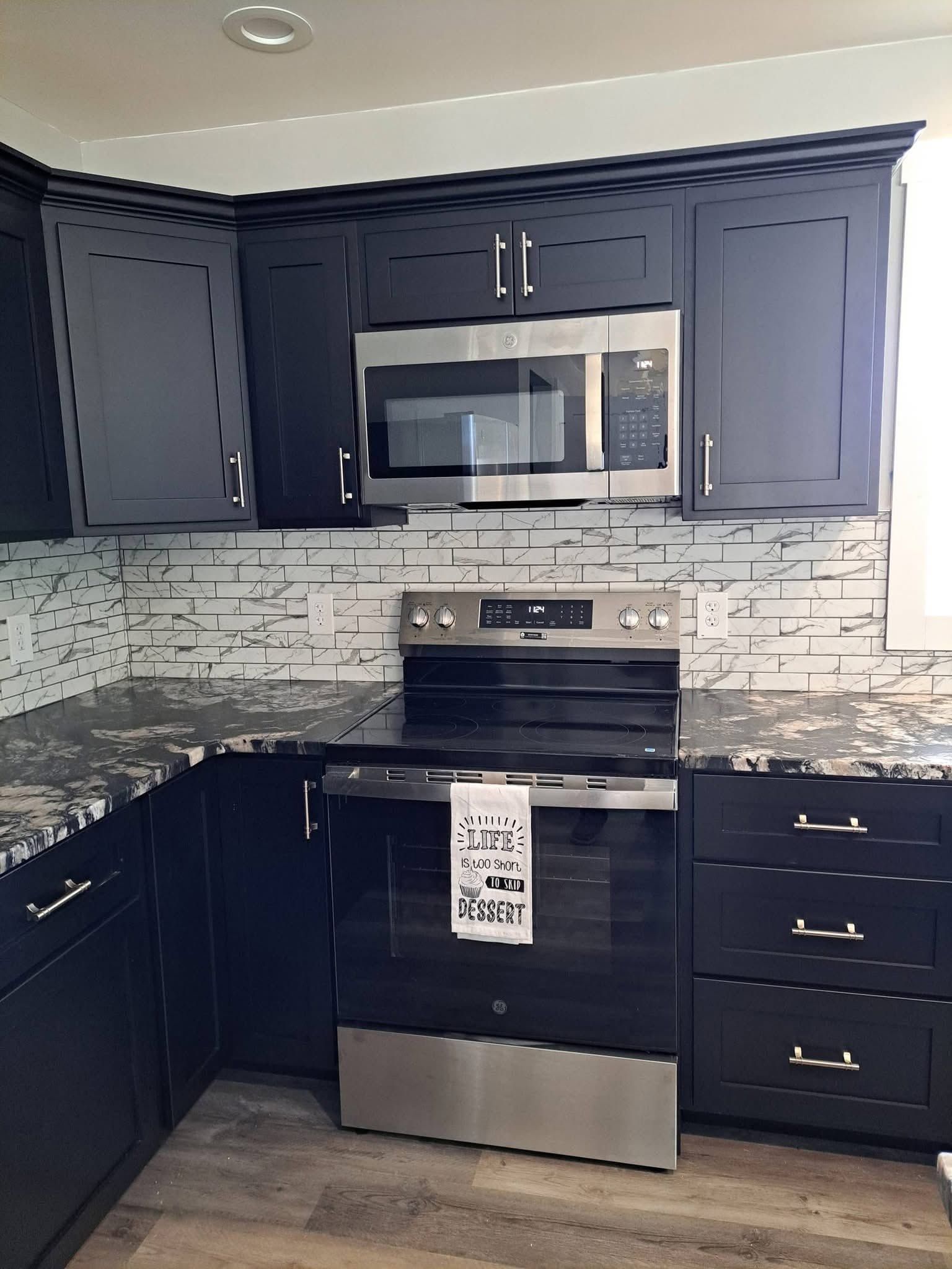 Modern kitchen with dark cabinets, stainless steel appliances, and white tile backsplash