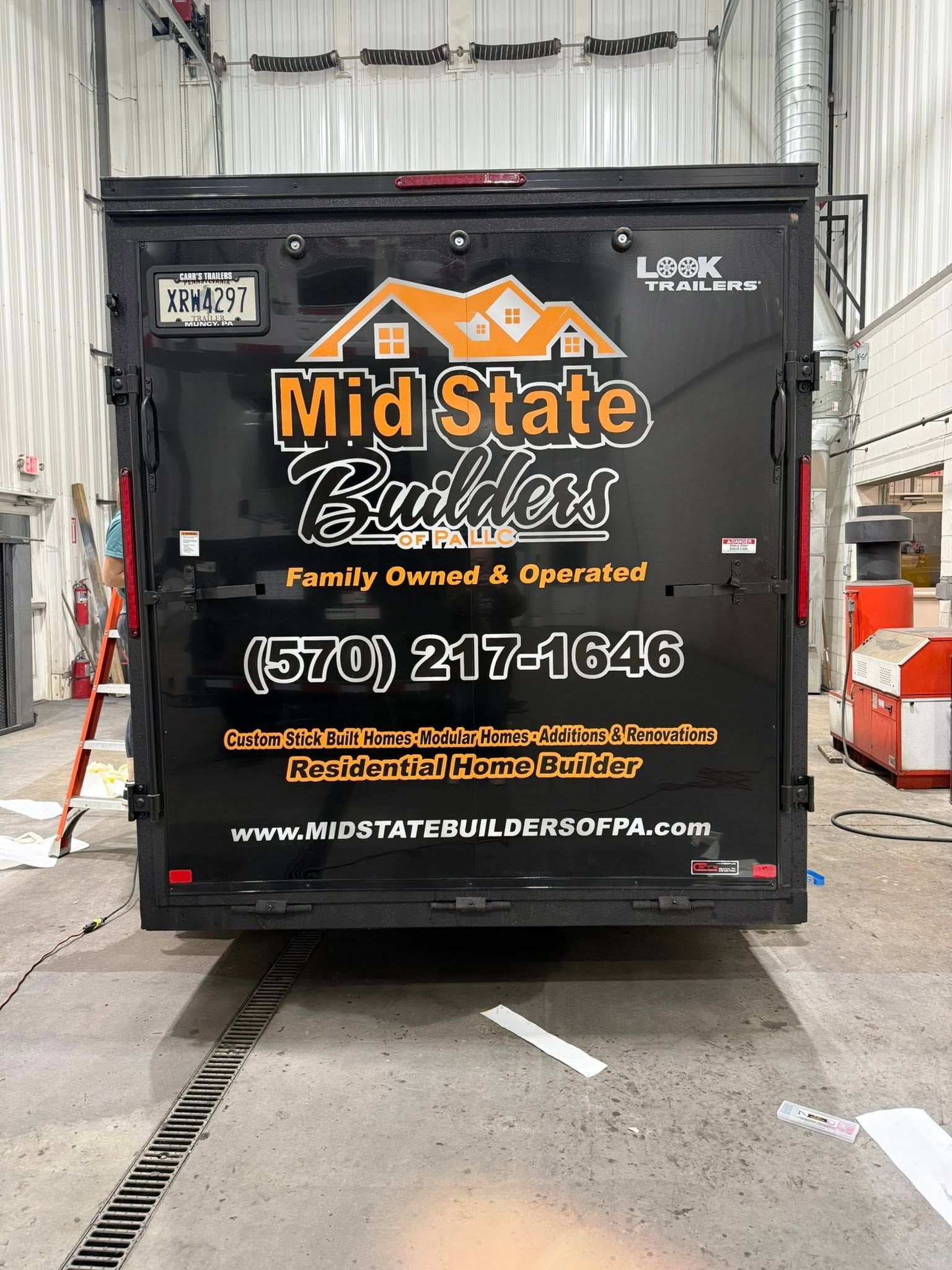 Black Mid State Builders delivery trailer with orange logo parked in a warehouse loading area.