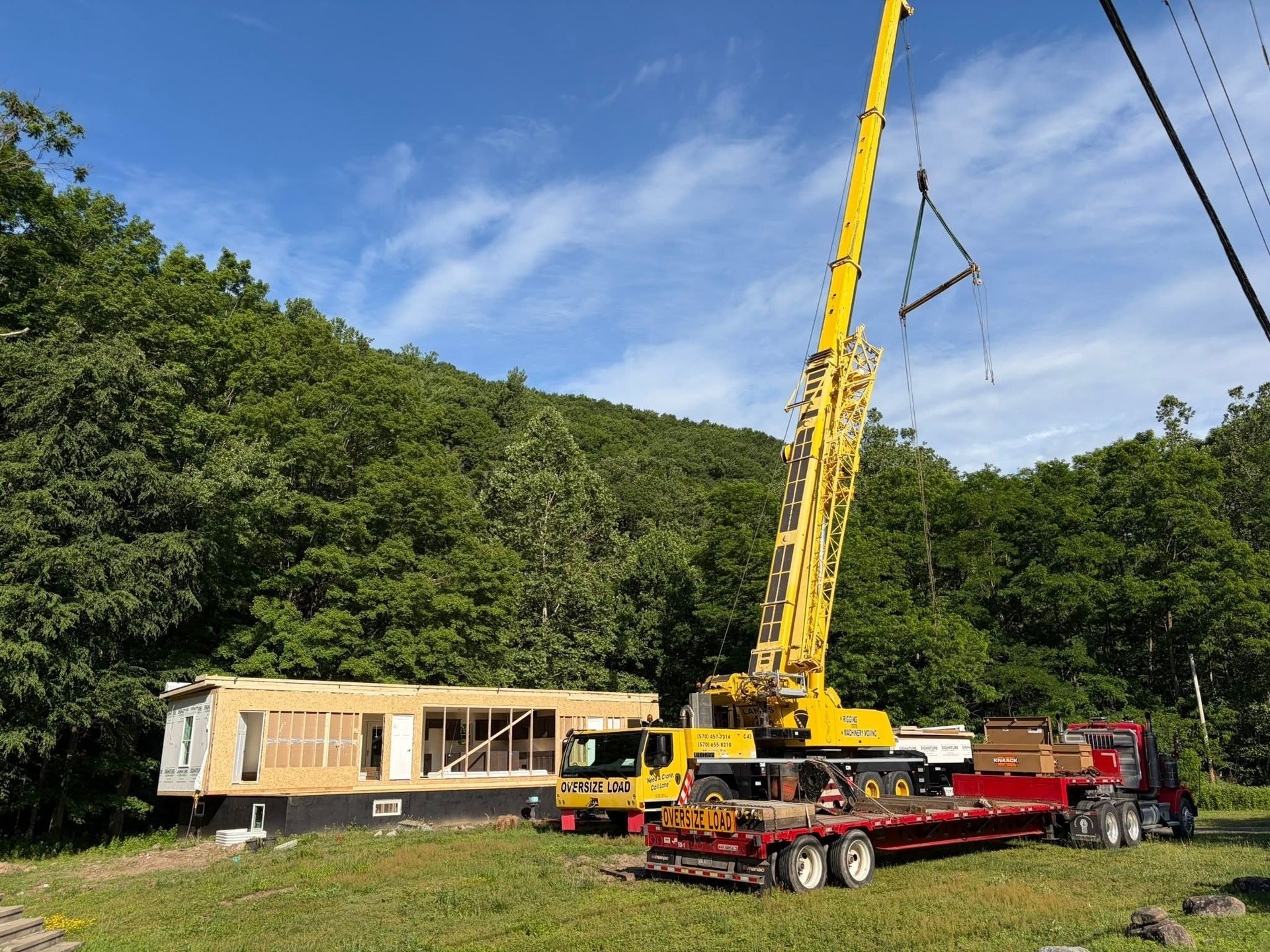 Yellow crane beside a mobile home under construction in a wooded area