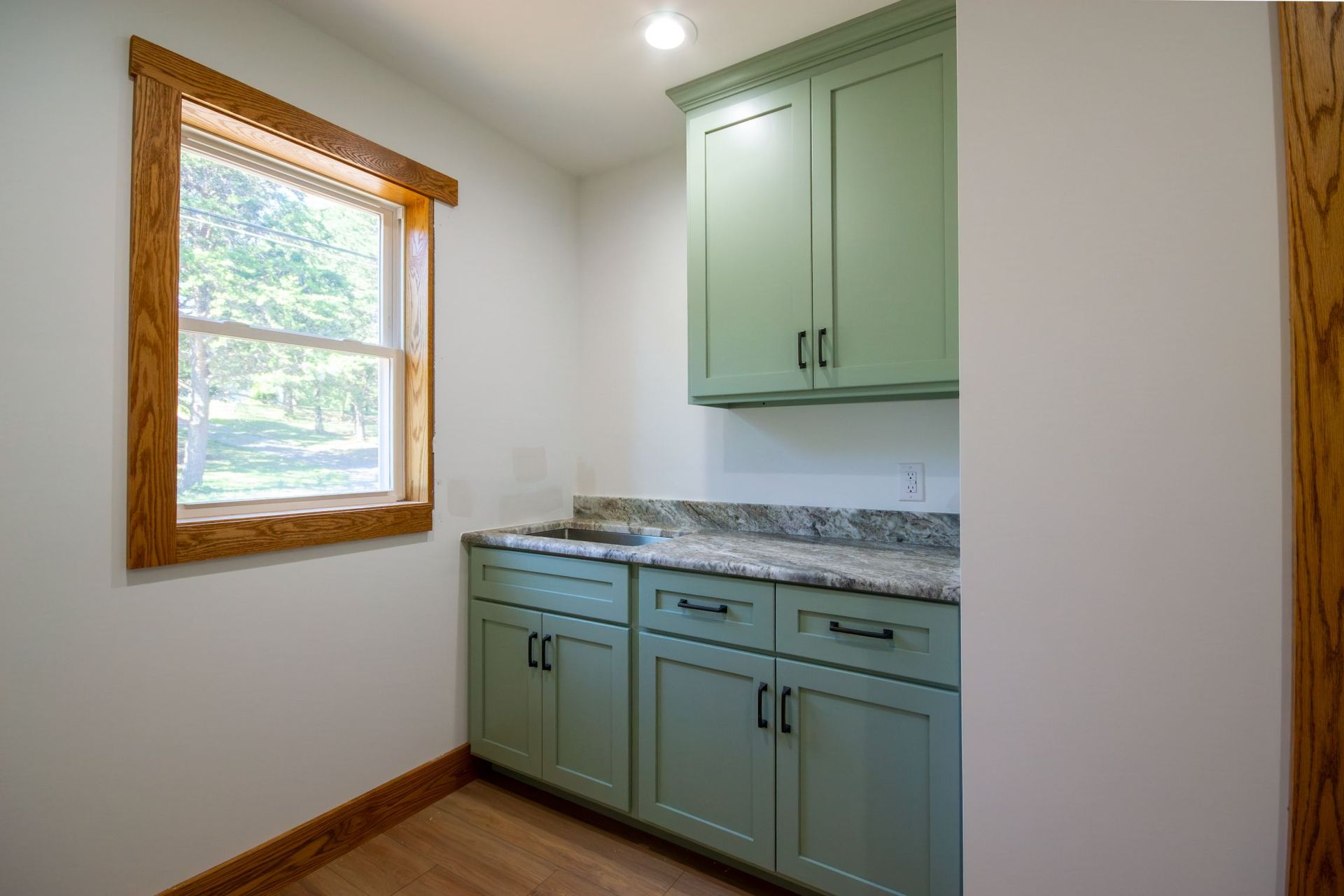Small kitchen nook with mint green cabinets, granite countertop, and a window with wood trim.