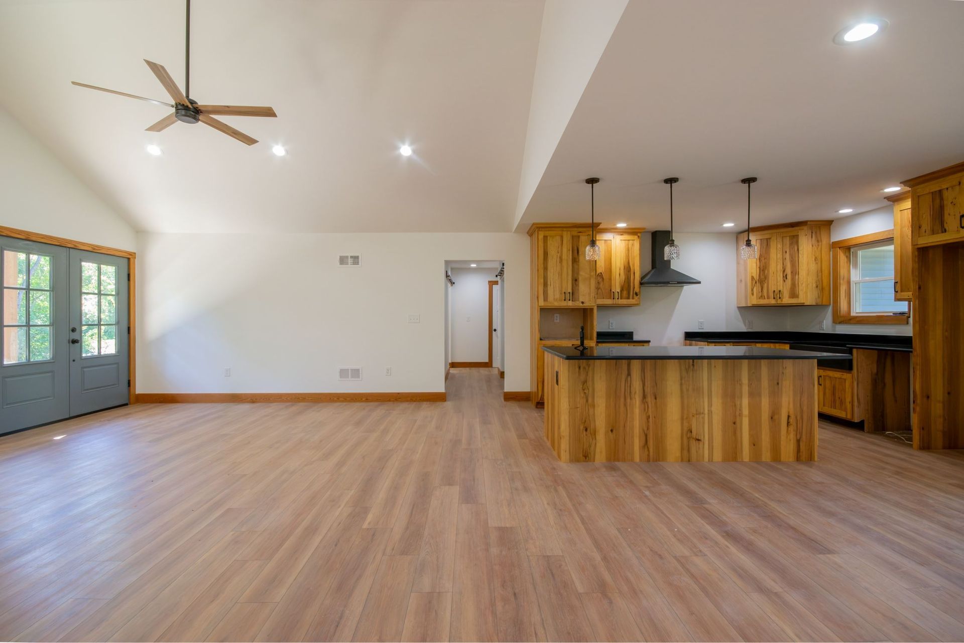 Spacious open-plan kitchen and living room with wood floors, island, ceiling fan, and large windows.