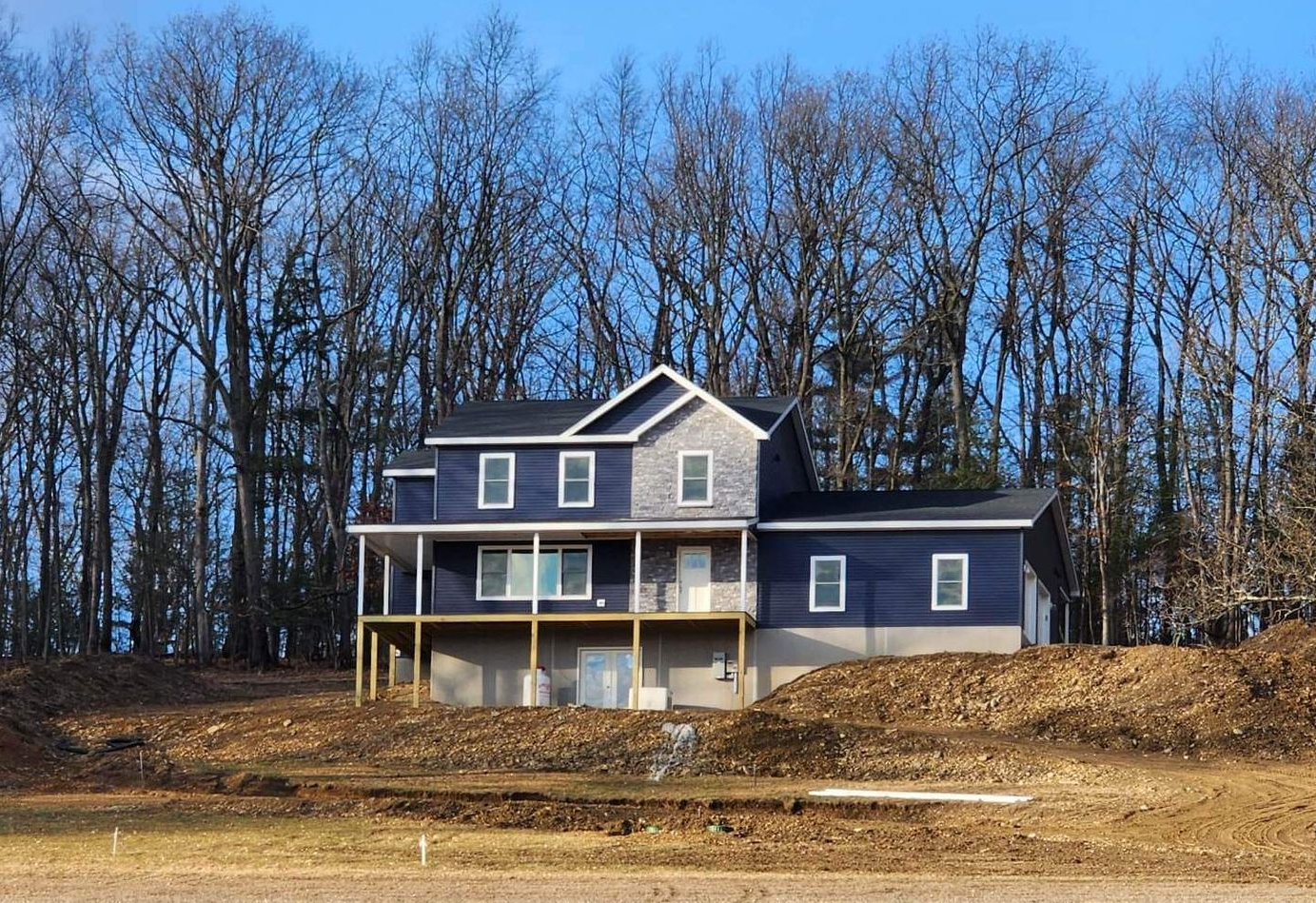 Blue two-story house with white trim on a bare hillside, backed by leafless trees under a clear sky.