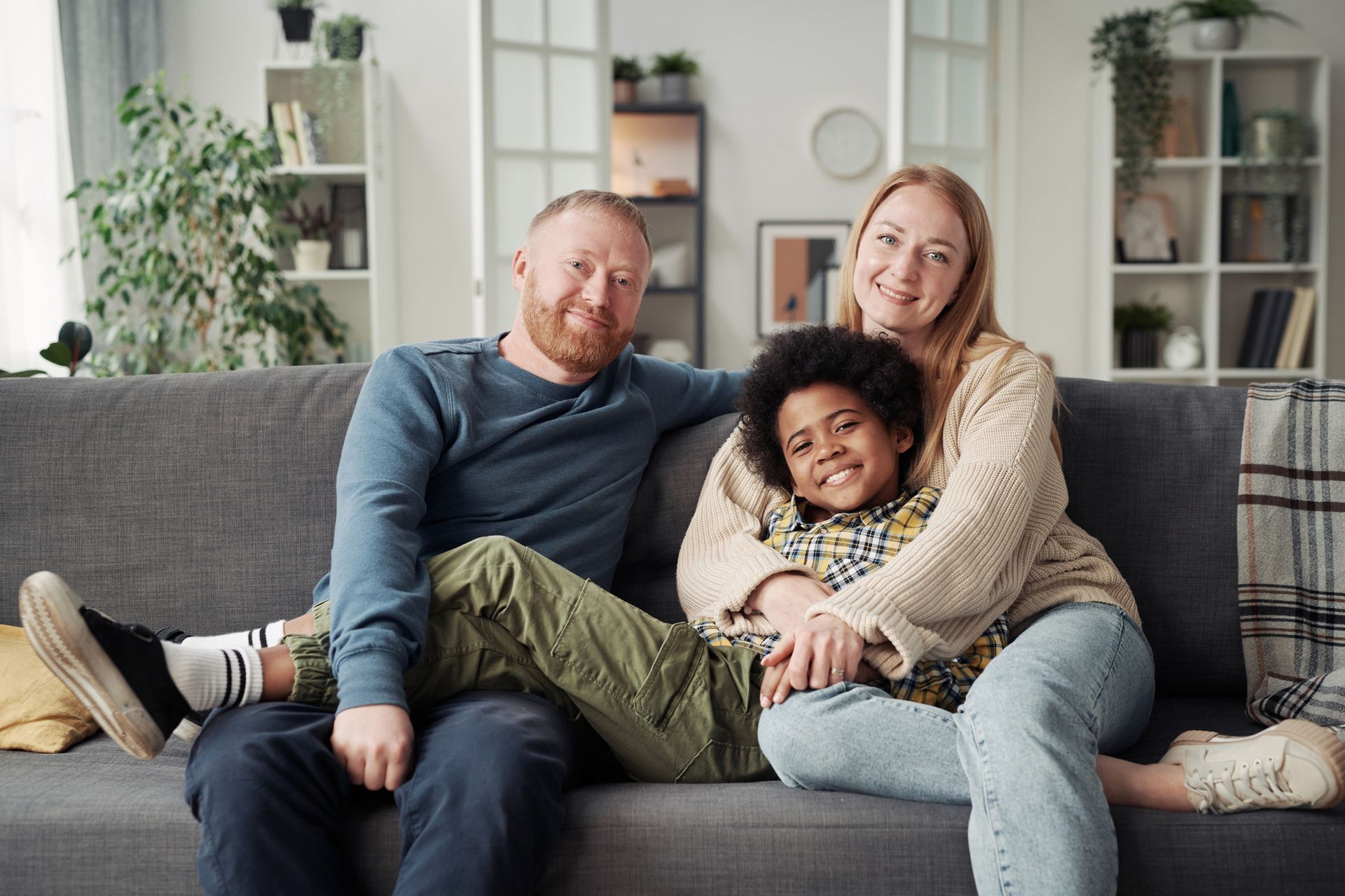 Pair of foster parents sit on grass smiling and hugging foster child, representing foster parenting.