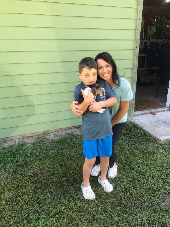 A woman is standing next to a boy holding a puppy.