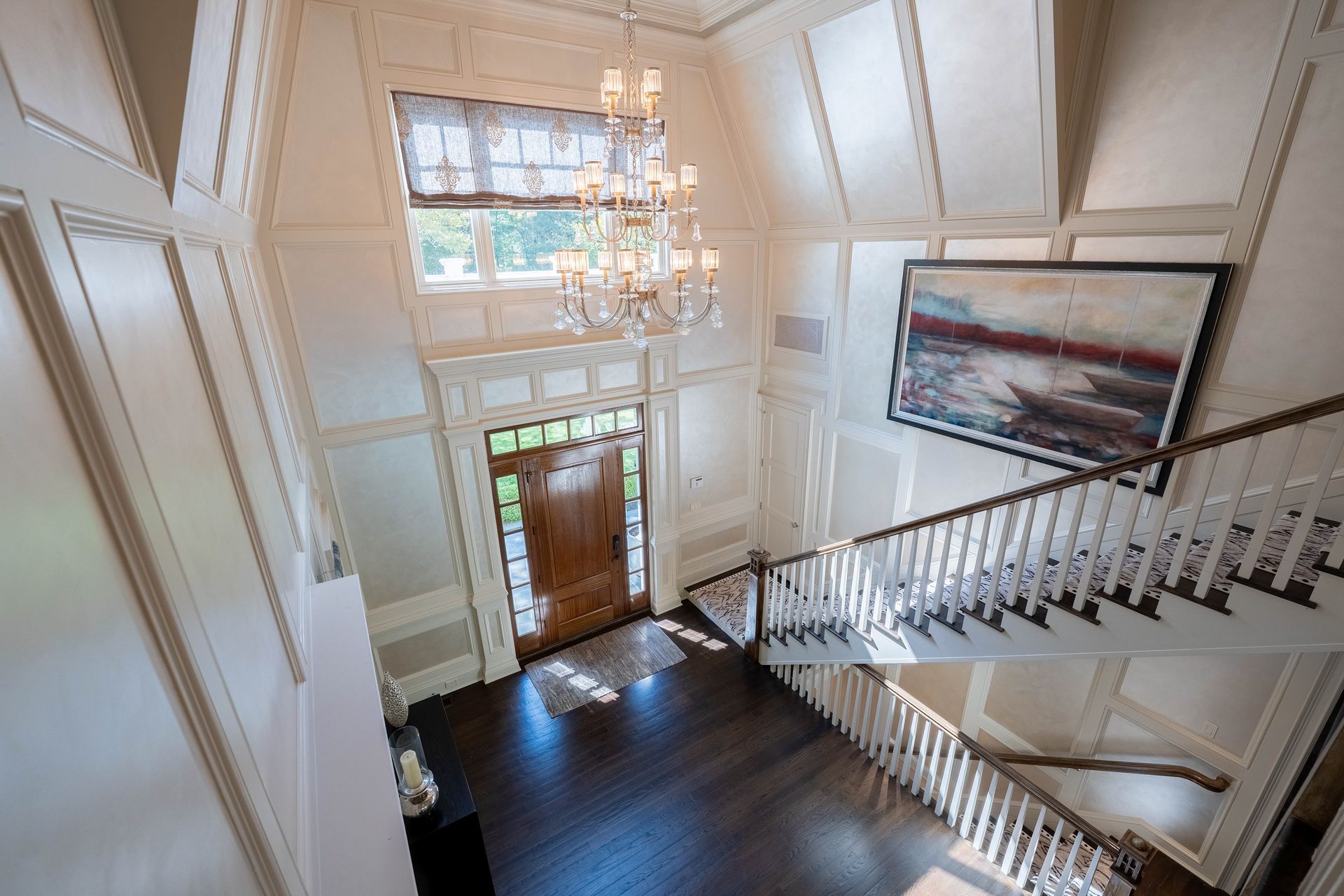 A grand foyer featuring a high ceiling, a large crystal chandelier, wood floors, a wooden front door, and a staircase.