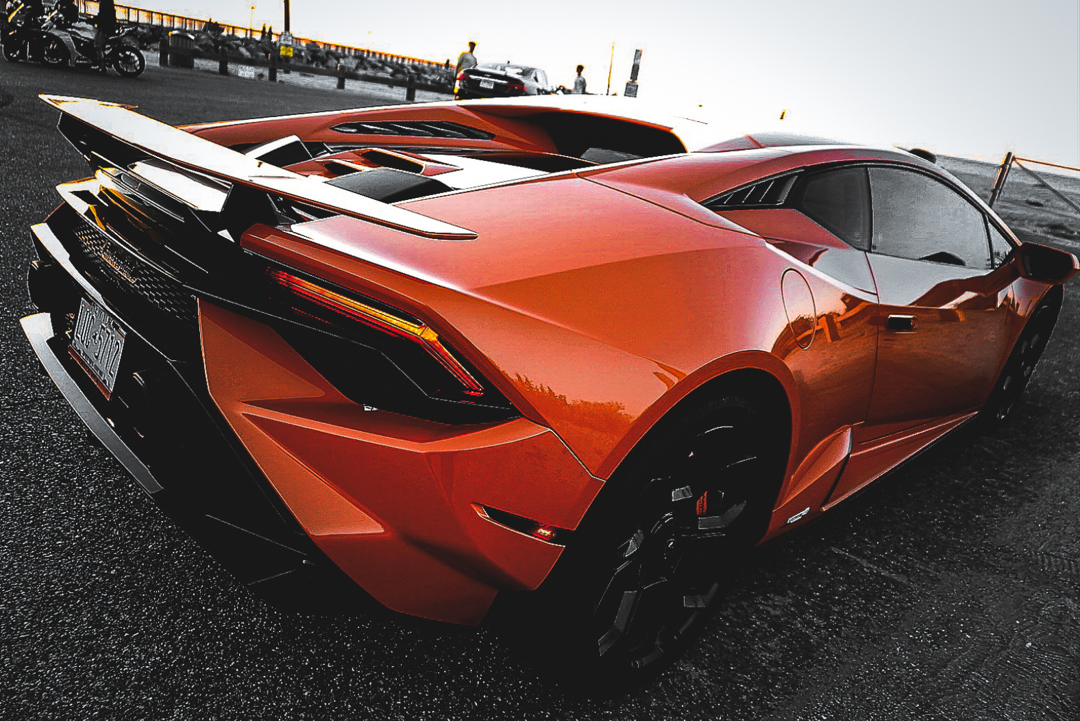 A bright orange Lamborghini sports car parked on an asphalt surface, viewed from the rear three-quarter angle.