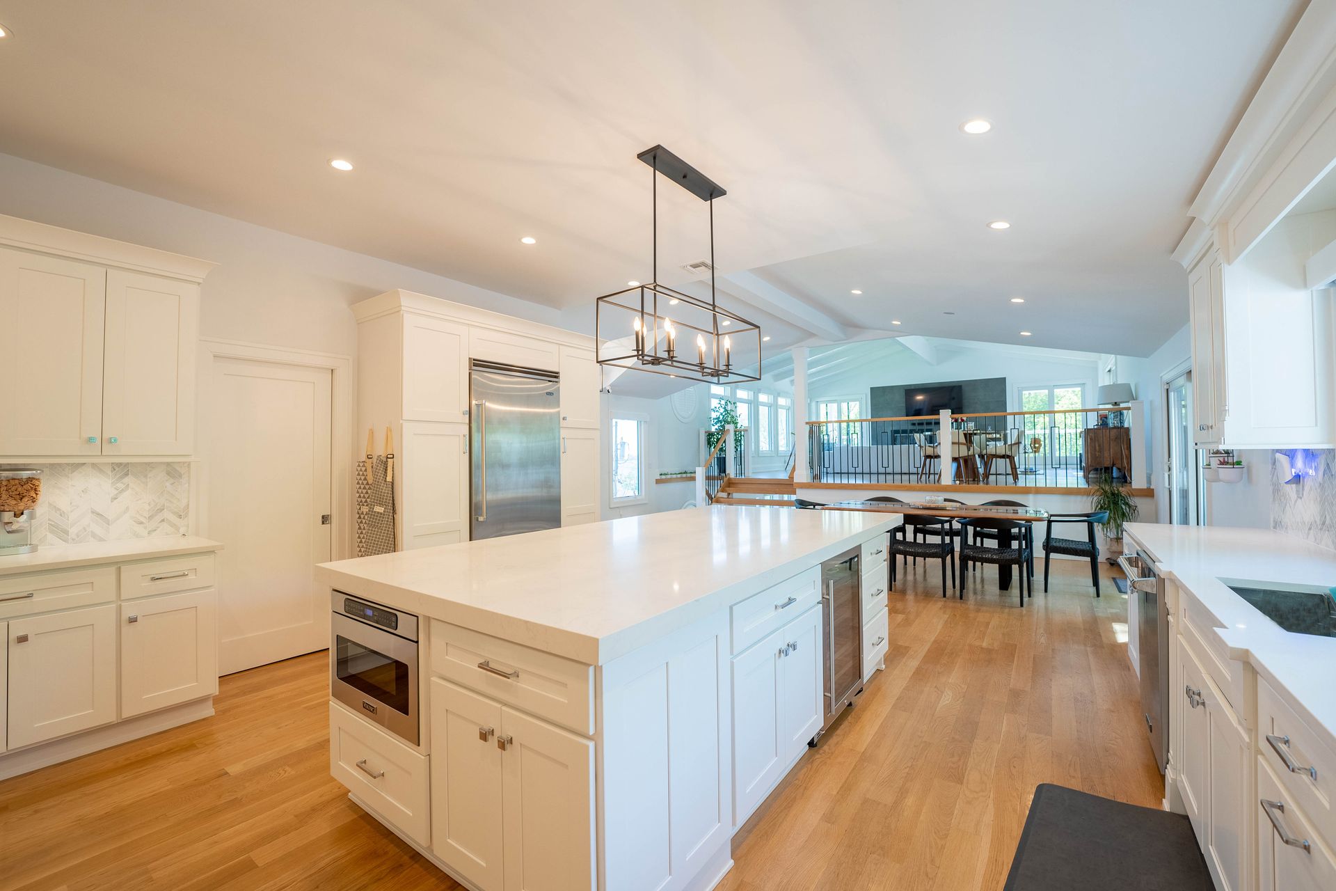 A bright, modern kitchen with white cabinets, a large central island, light wood floors, and a hanging pendant light.