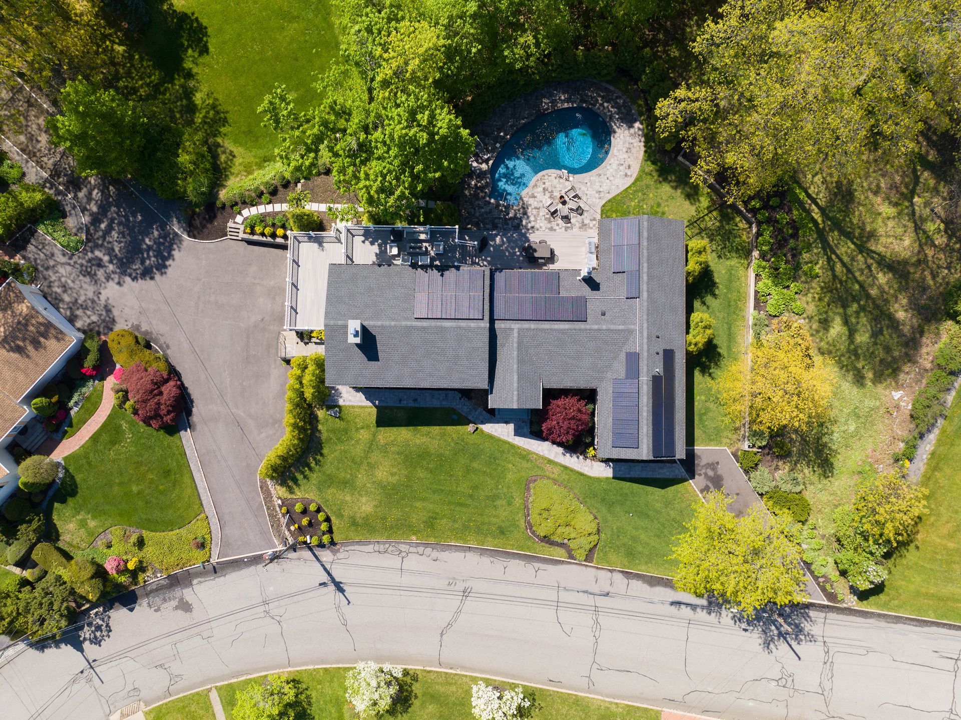 Aerial view of a residential house with a dark shingled roof, solar panels, and a backyard swimming pool.