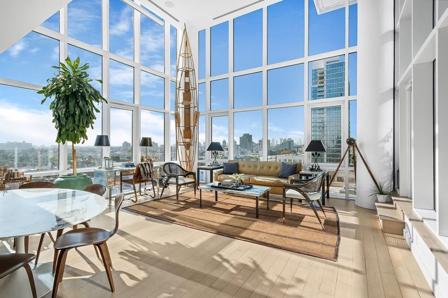 Modern high-rise living room with floor-to-ceiling windows, city views, a seating area, and a decorative pillar.