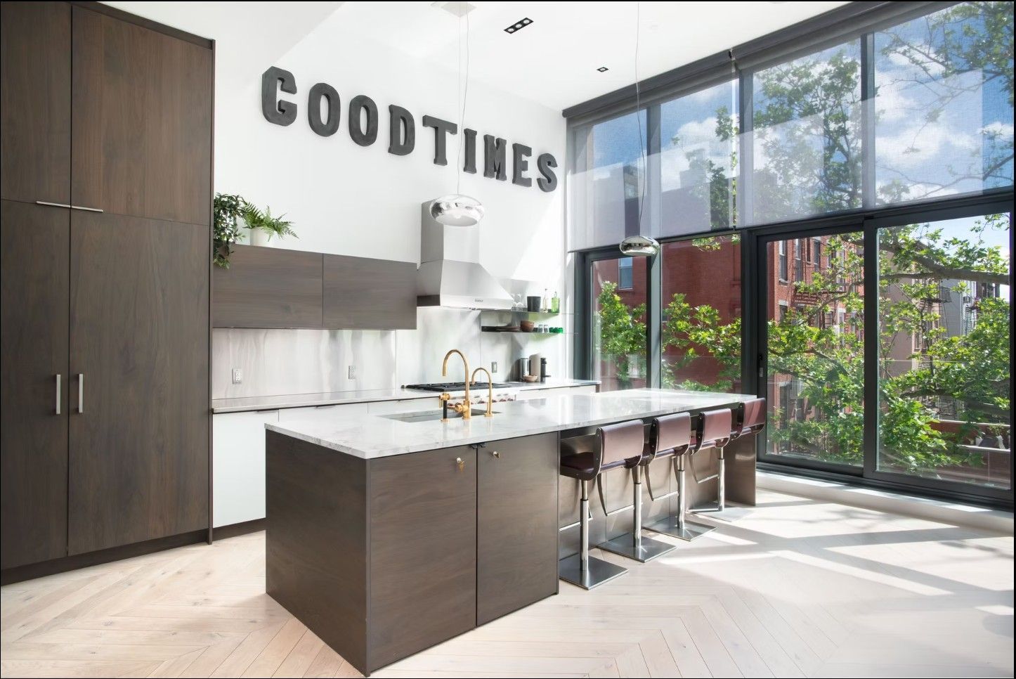 Modern kitchen with dark wood cabinets, a large white stone island, bar stools, and floor-to-ceiling windows.