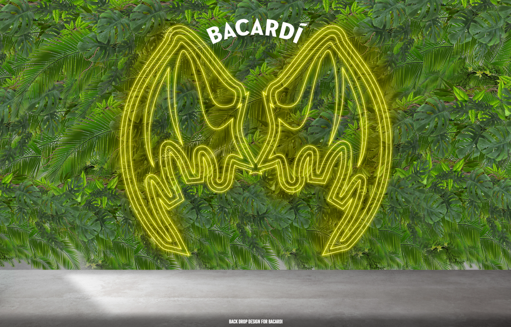 A yellow neon Bacardi bat logo mounted on a vibrant green leafy wall above a flat, gray concrete surface.