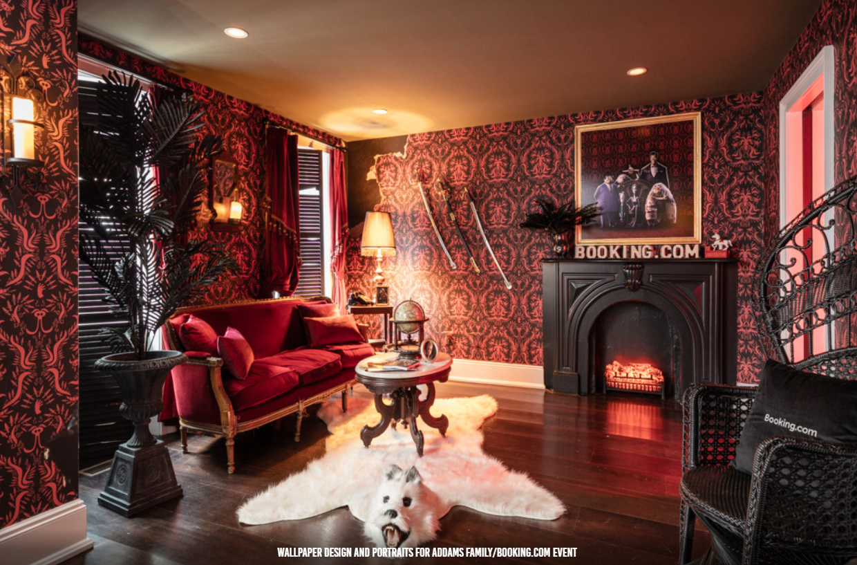 A dimly lit, opulent room featuring red velvet furniture, dark damask wallpaper, a fireplace, and a faux fur rug.
