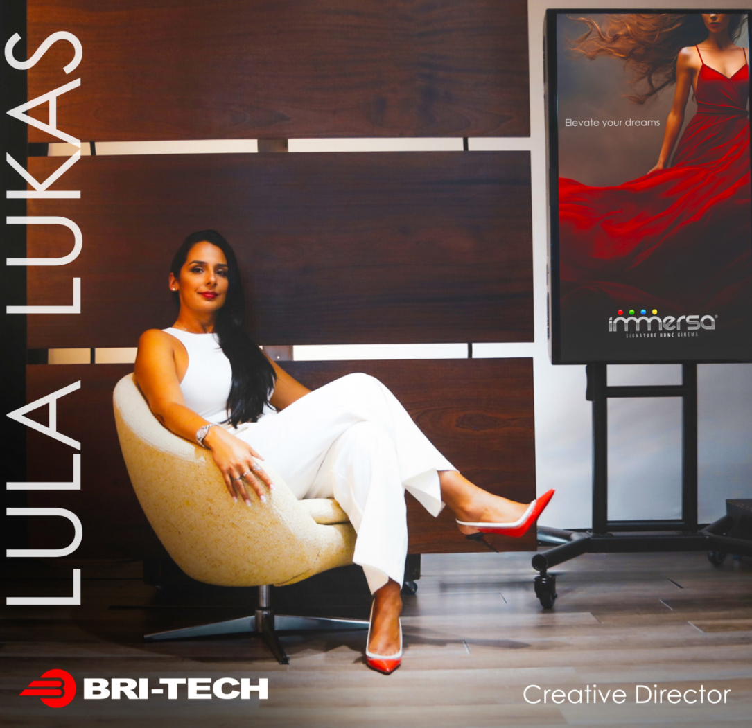 Lula Lukas, Creative Director at BRI-TECH, sits in a chair in an office next to a monitor displaying an Immersa ad.