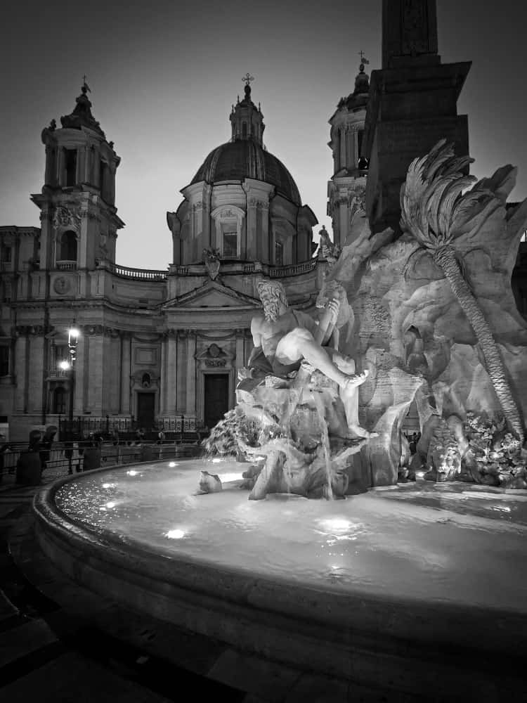 Black and white photo of the Fountain of the Four Rivers and Sant'Agnese in Agone church in Rome at twilight.