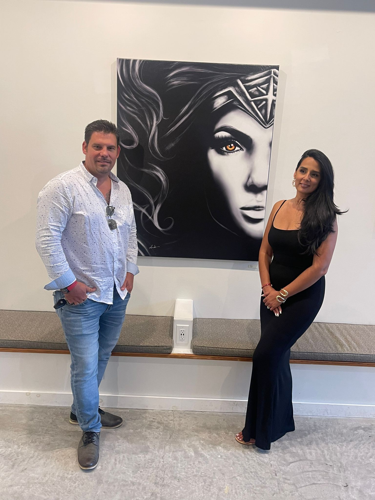 A man and woman standing on either side of a large portrait of Wonder Woman in a gallery space.