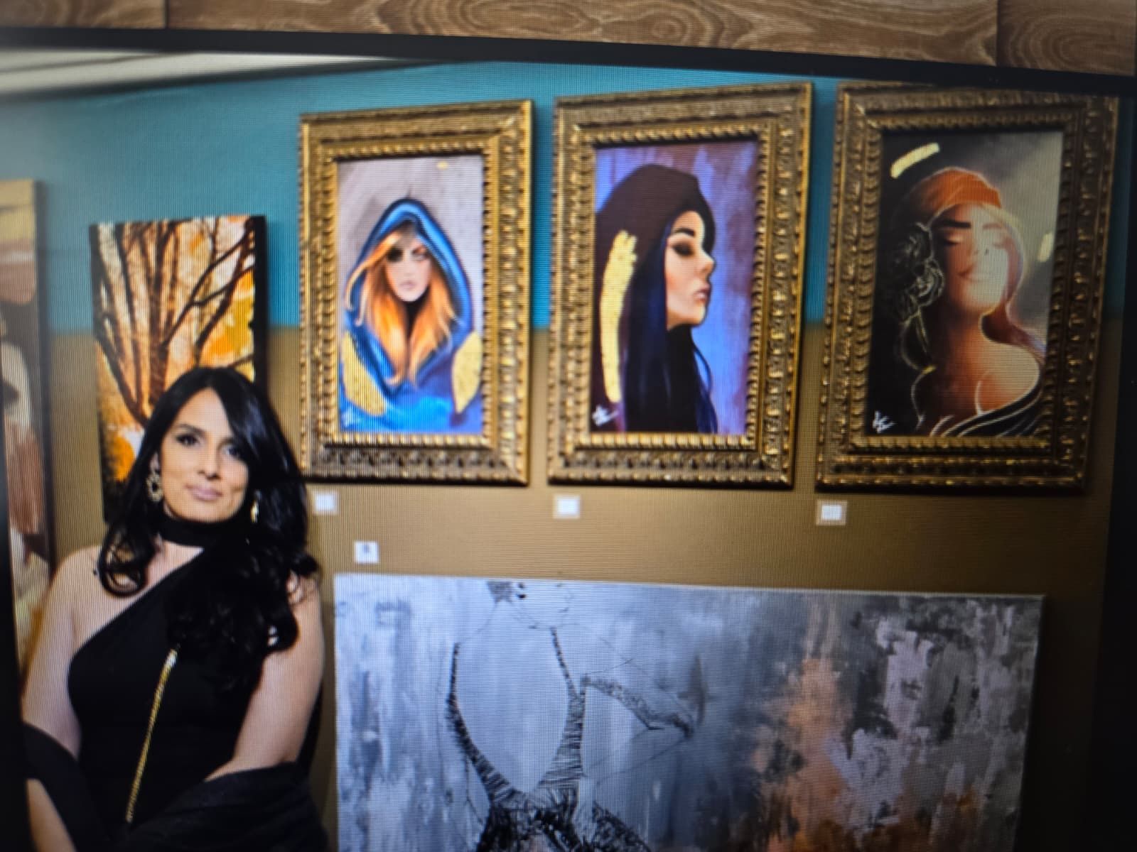 A person stands in an art gallery beside a wall displaying four framed paintings of faces and abstract scenes.