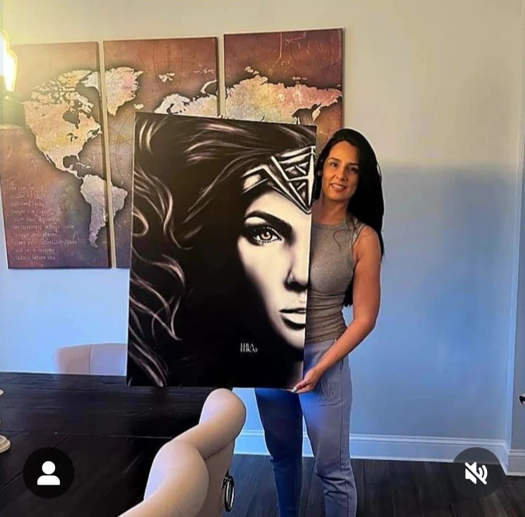 A person stands in a room holding a large, black-and-white portrait of Wonder Woman in front of their face.