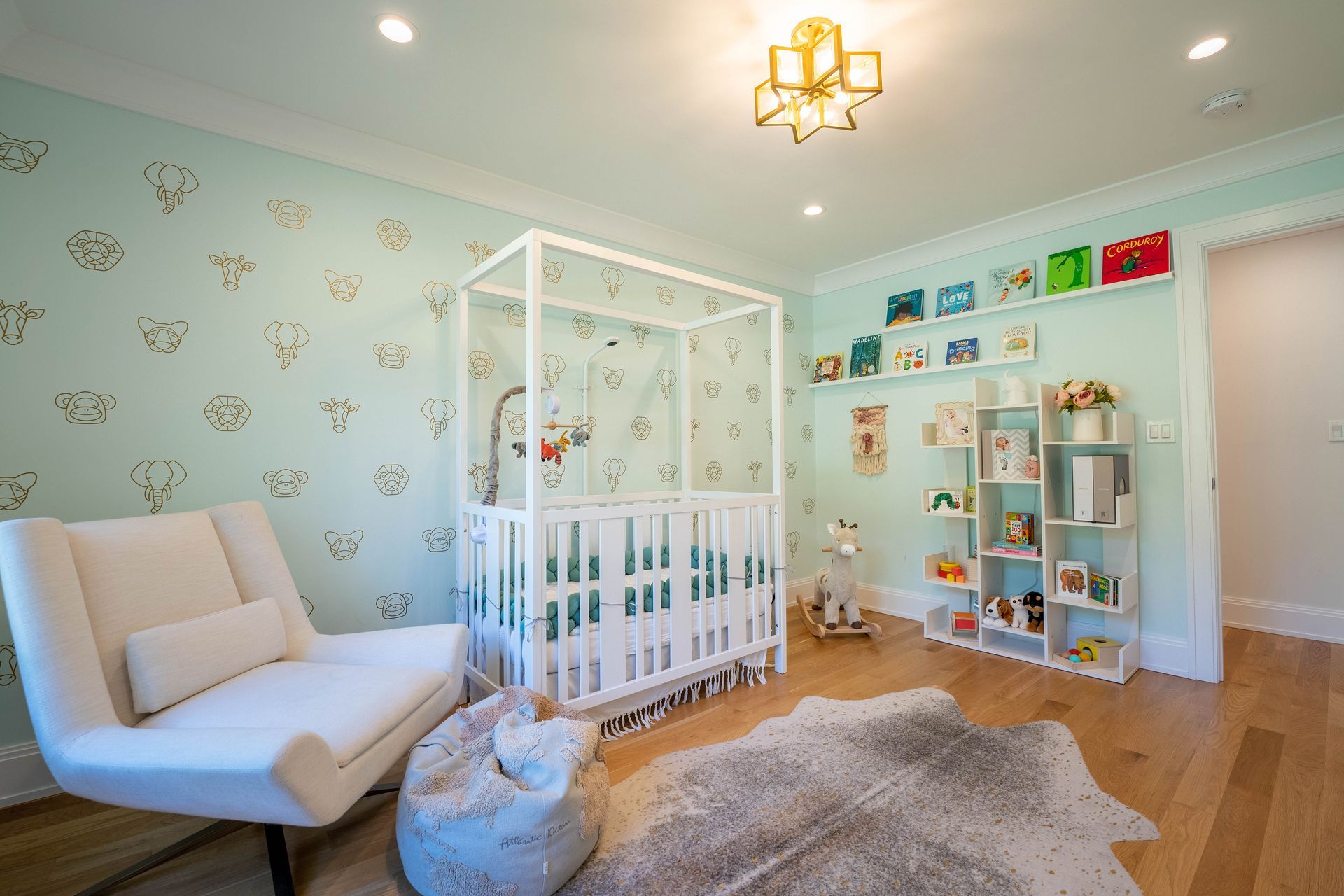 A nursery with light blue patterned wallpaper, a white crib, a white armchair, a bookshelf, and a grey cowhide rug.