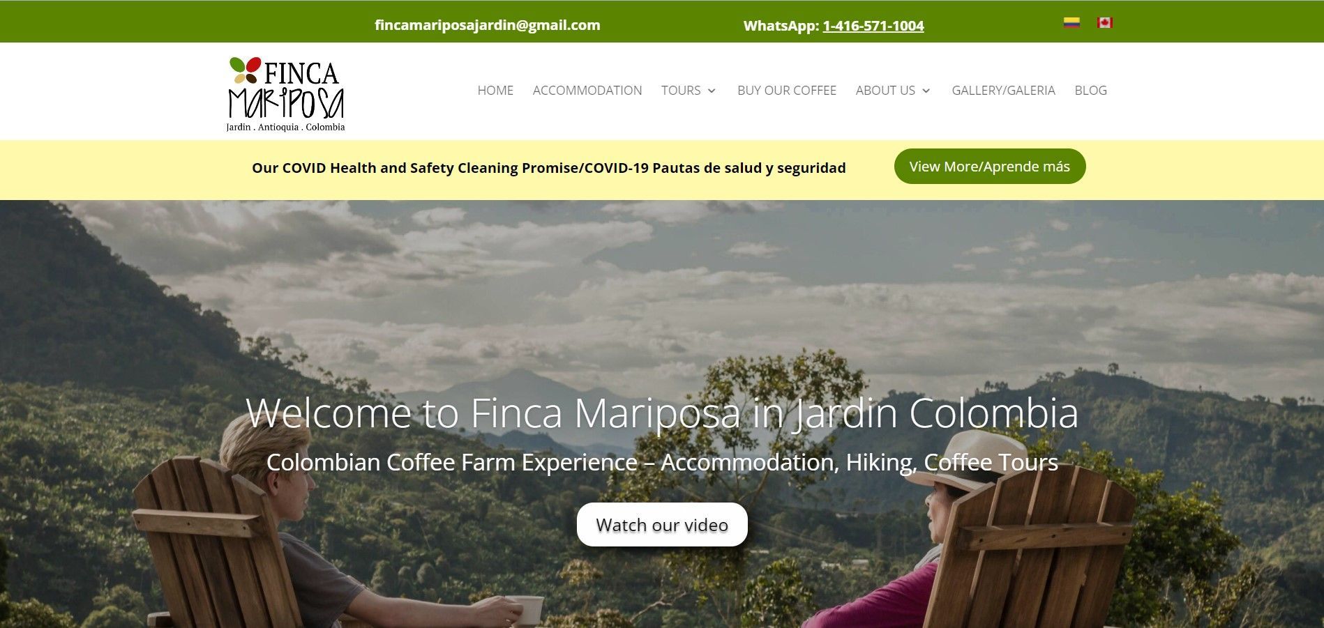 Two people sit in wooden chairs overlooking a lush, mountainous Colombian coffee landscape on the Finca Mariposa website.