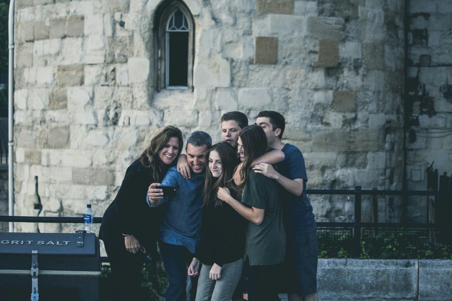 A group of five people poses for a selfie in front of a rustic stone wall with an arched window.